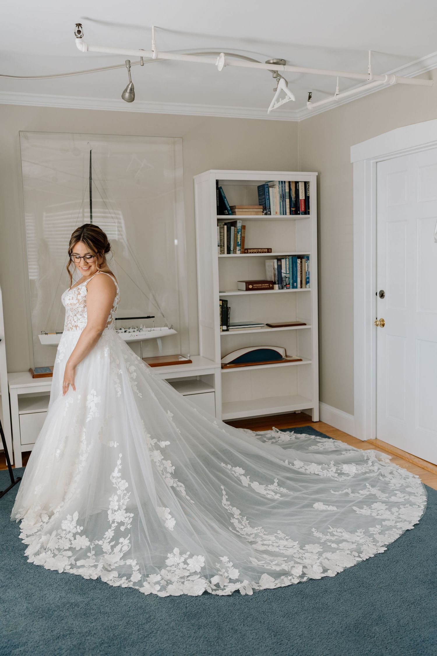 Wedding dress with dramatic lace train spread out on blue carpet.