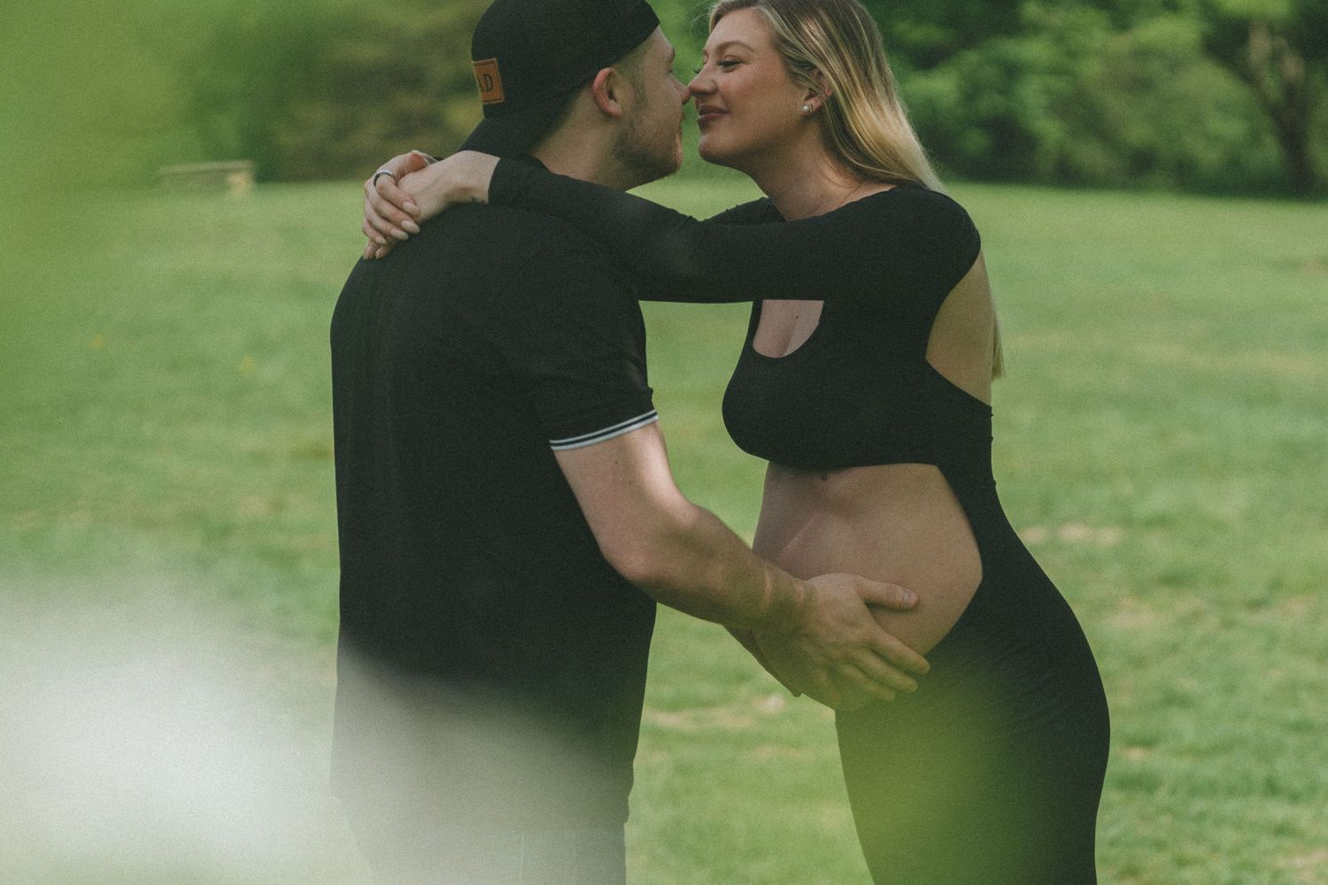 Romantic couple embraces in a lush green outdoor setting during a photo session.