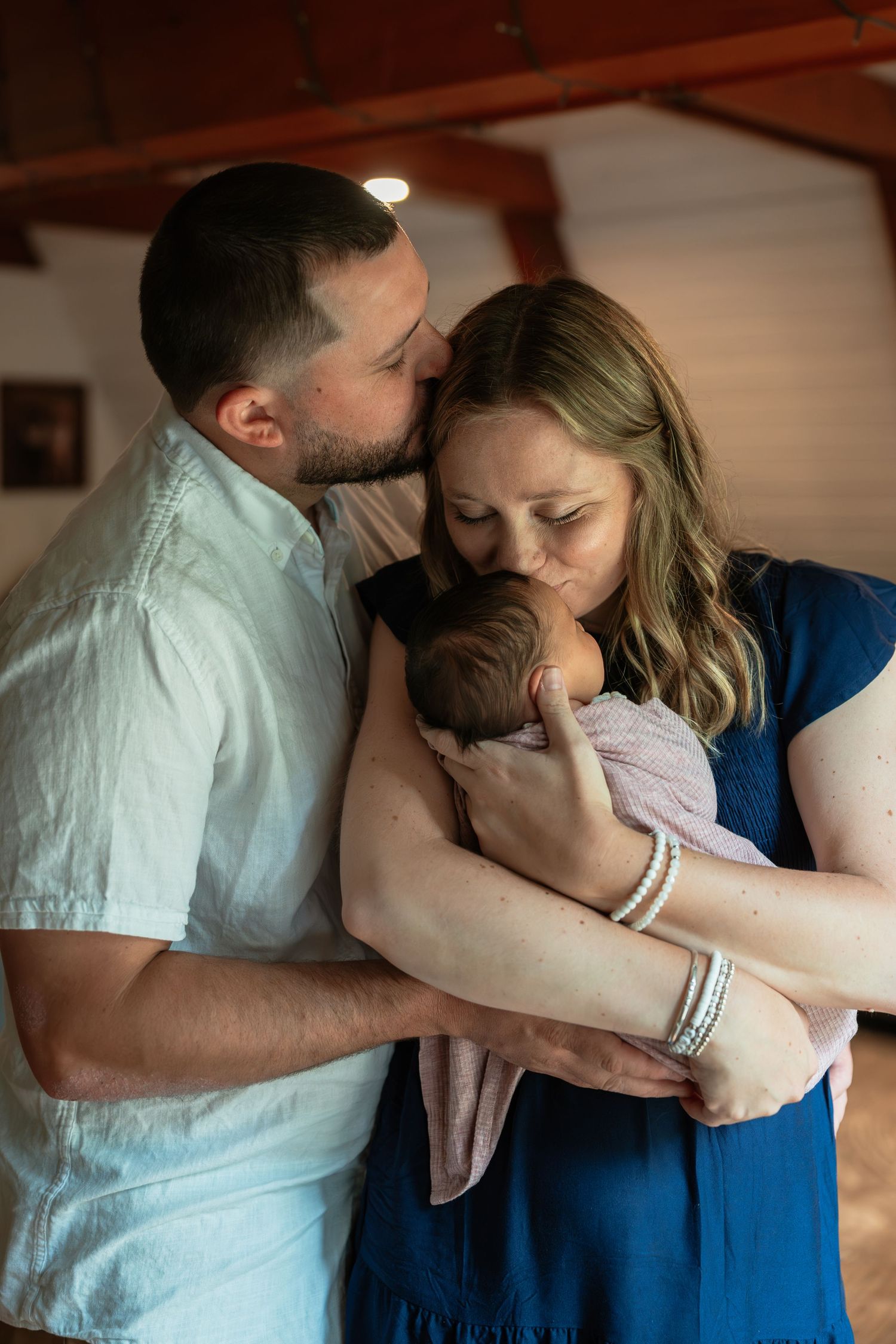 Intimate family moment captured in warm indoor lighting with exposed wooden beams.