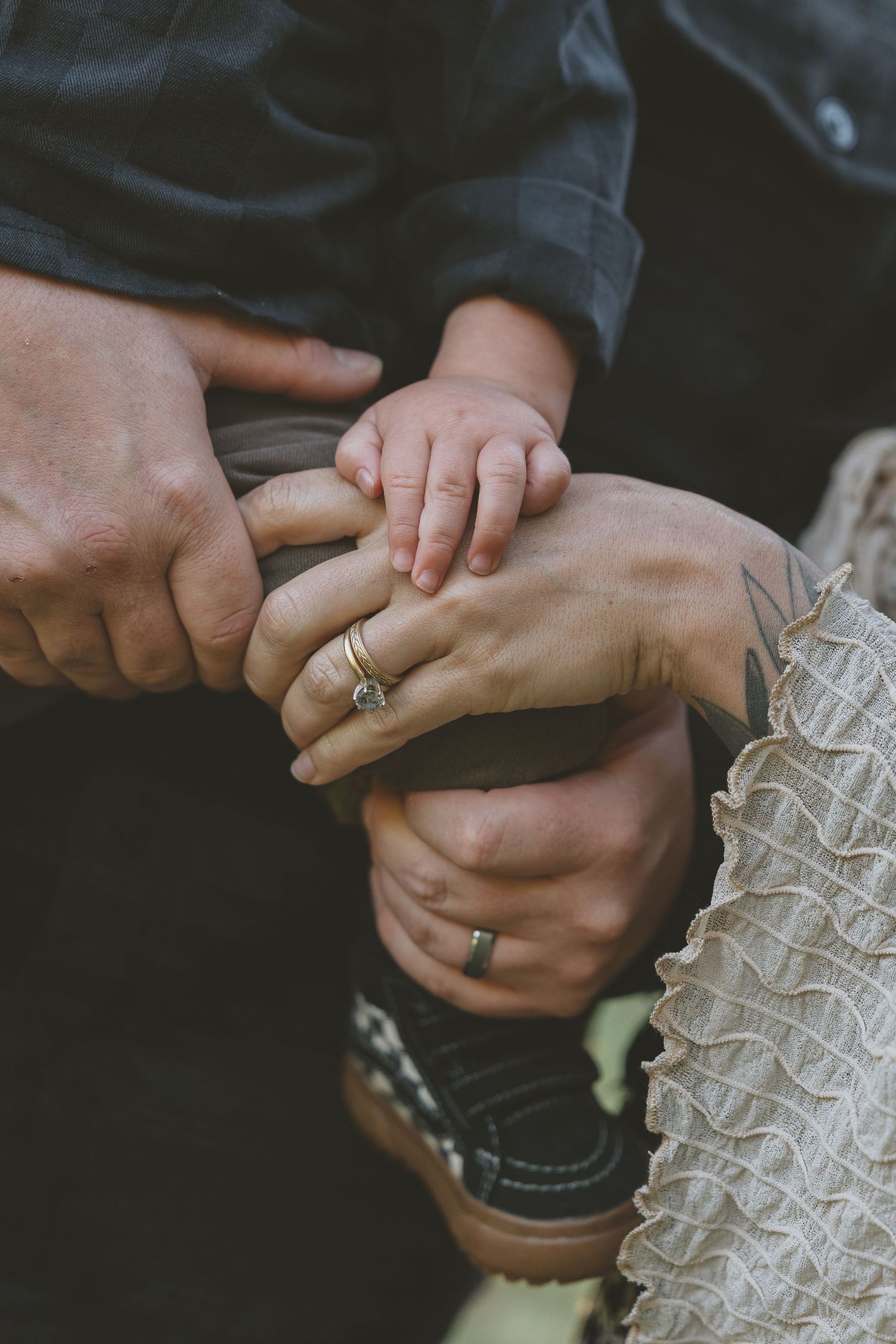 Close-up of hands holding each other tenderly showing wedding rings against a dark background.
