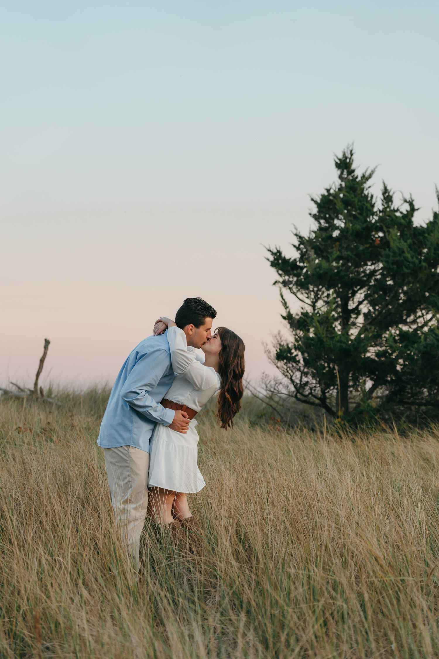 A romantic moment between a couple in a field of tall grass at dusk.