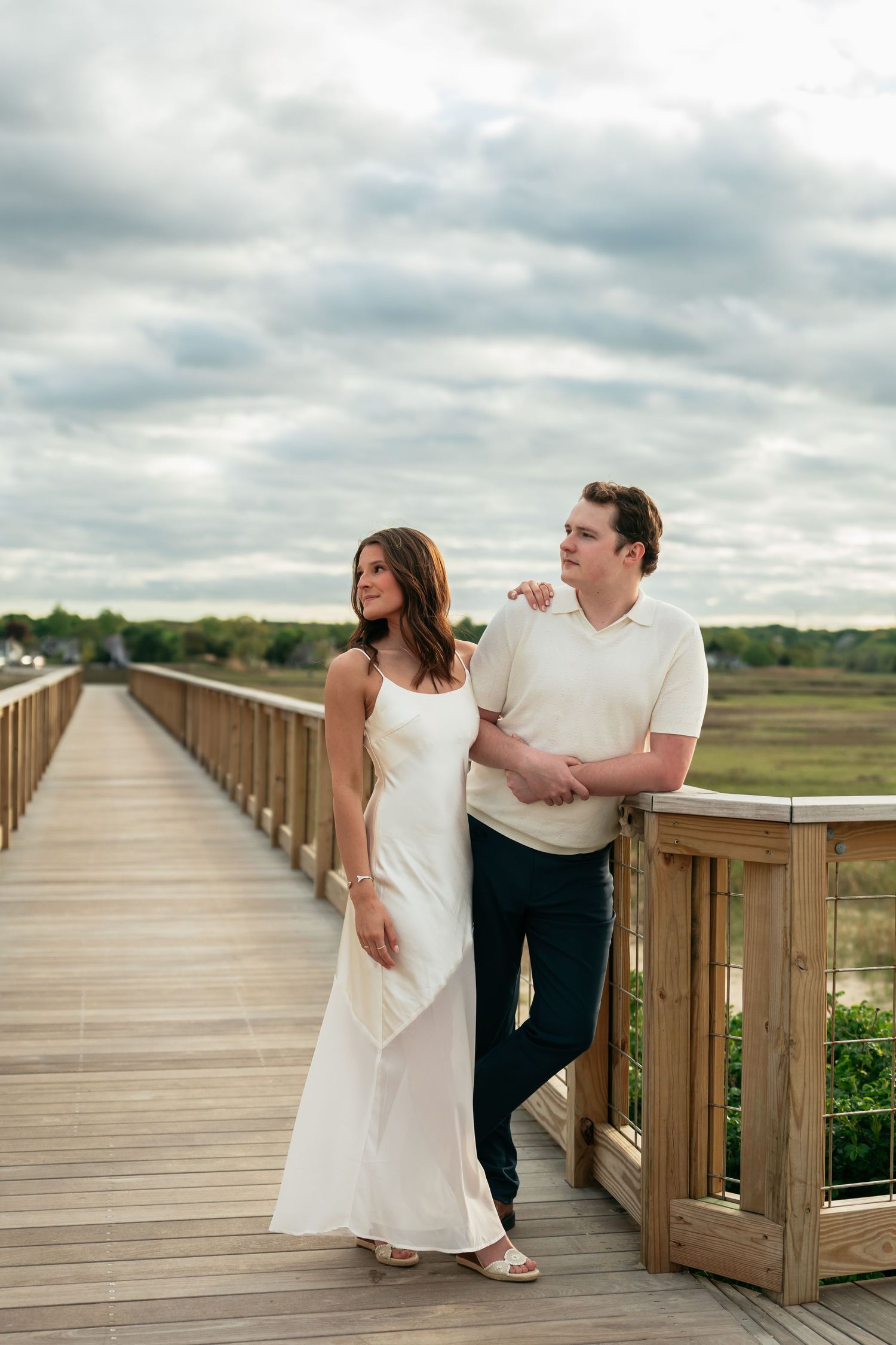 A couple walking together on a wooden boardwalk under cloudy skies.