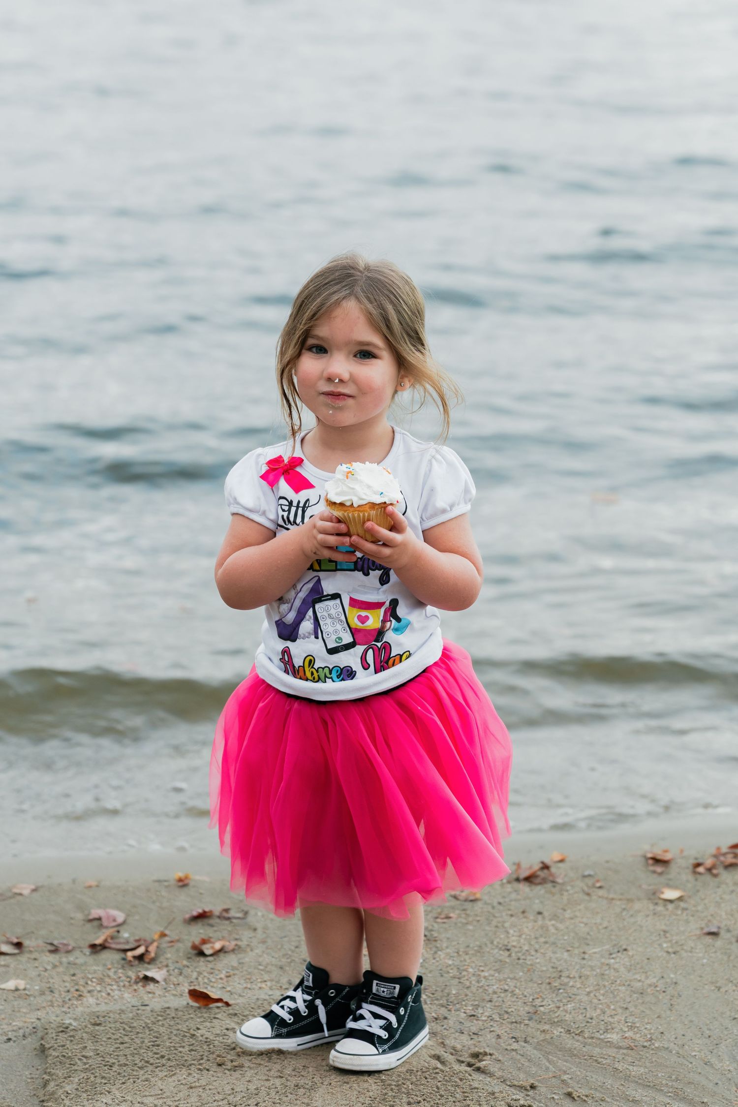 A bright pink tulle skirt stands out against the beach backdrop as a small figure enjoys a treat.