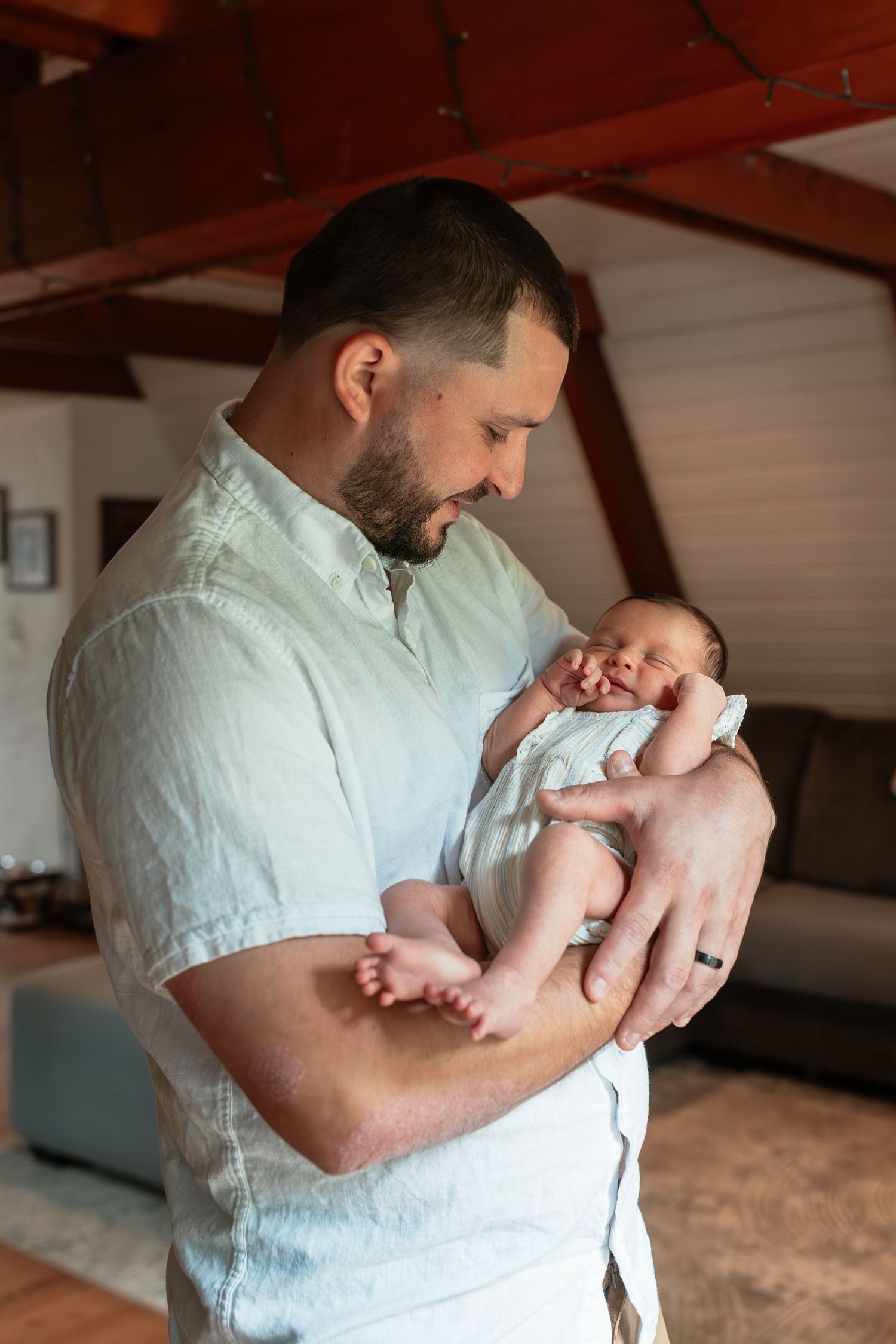 Parent holding and bonding with newborn baby in white shirt against wooden ceiling.