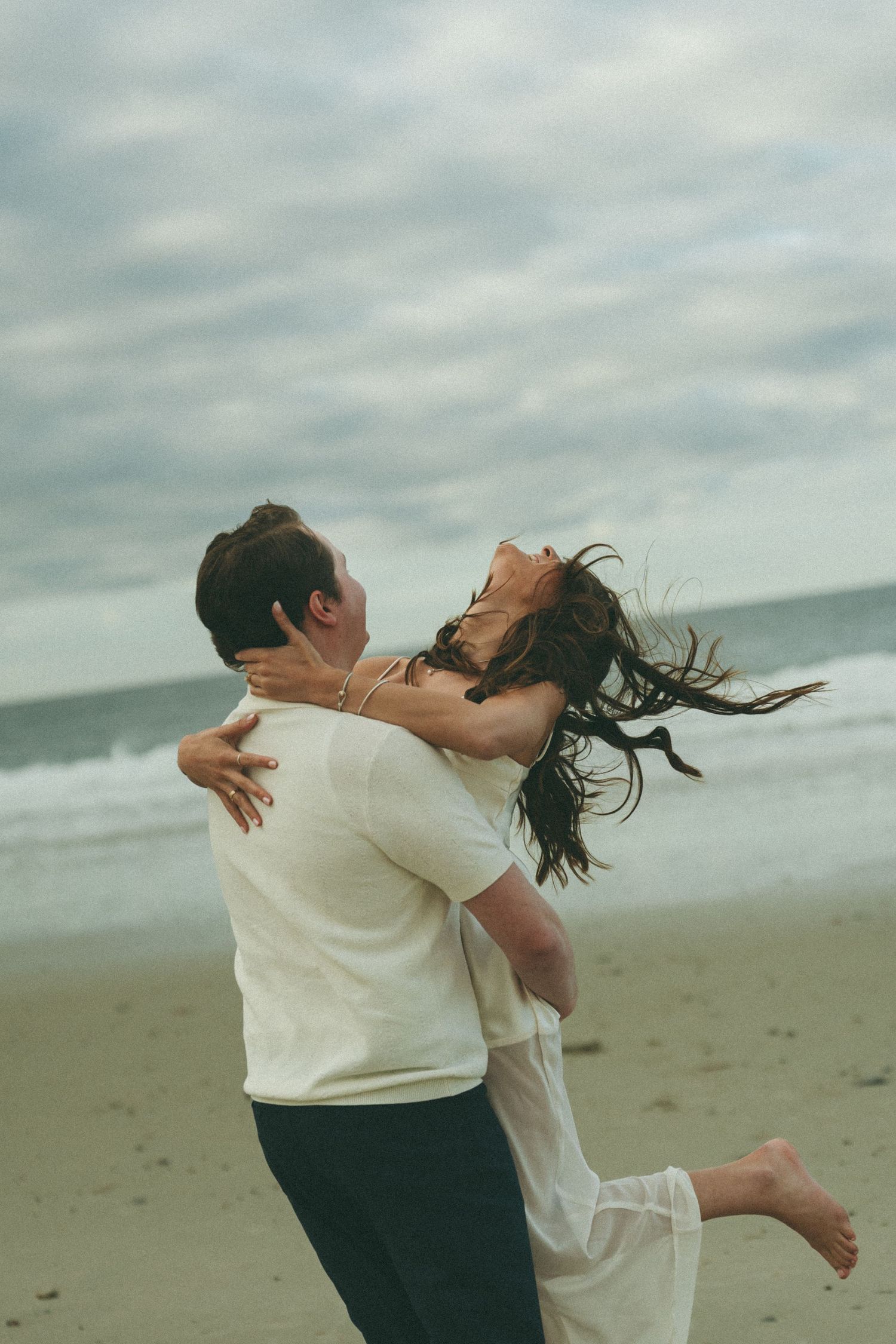 A romantic couple embracing and spinning on a cloudy beach.