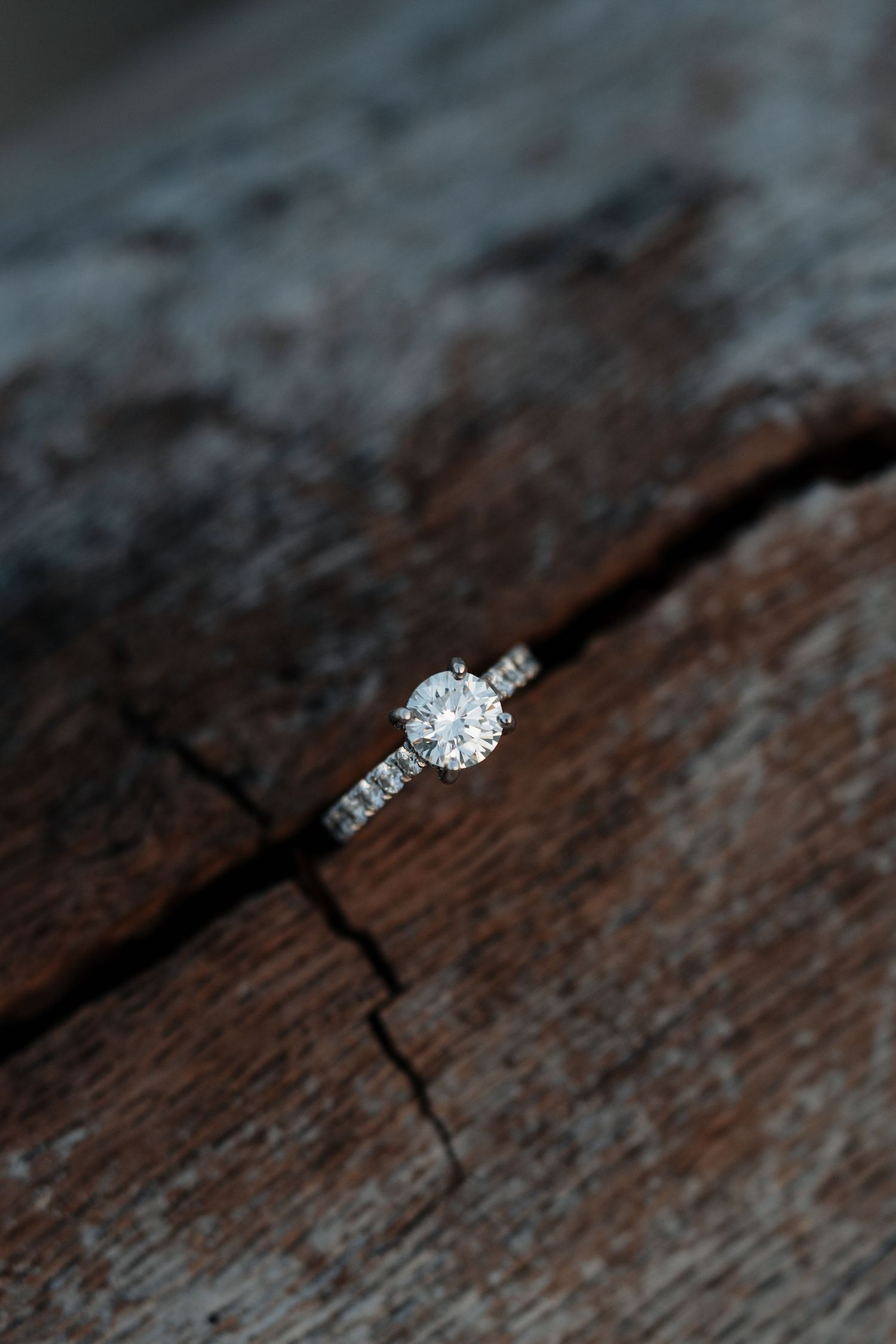 Close-up of a sparkling diamond engagement ring on weathered wood.