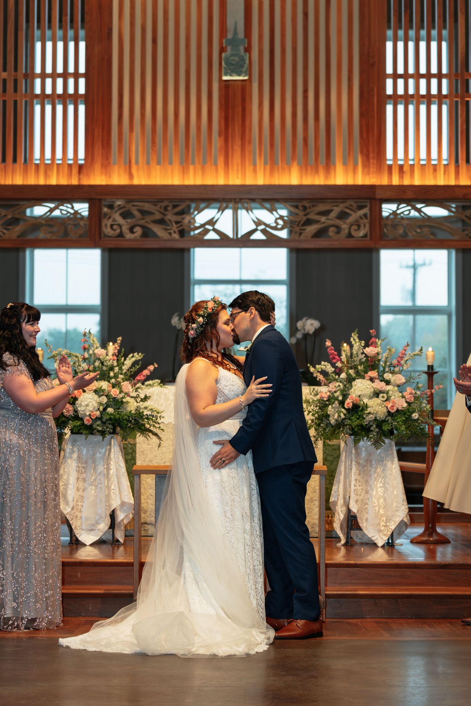 Wedding ceremony in a wooden paneled room with large windows and floral arrangements.