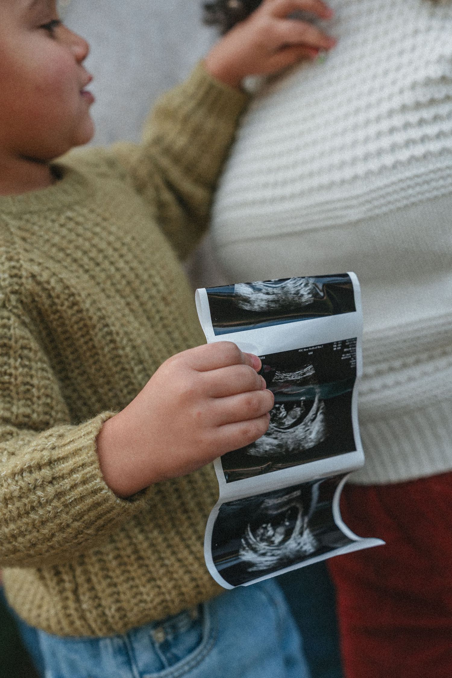 Child holding and examining an ultrasound photo while wearing a knit sweater.