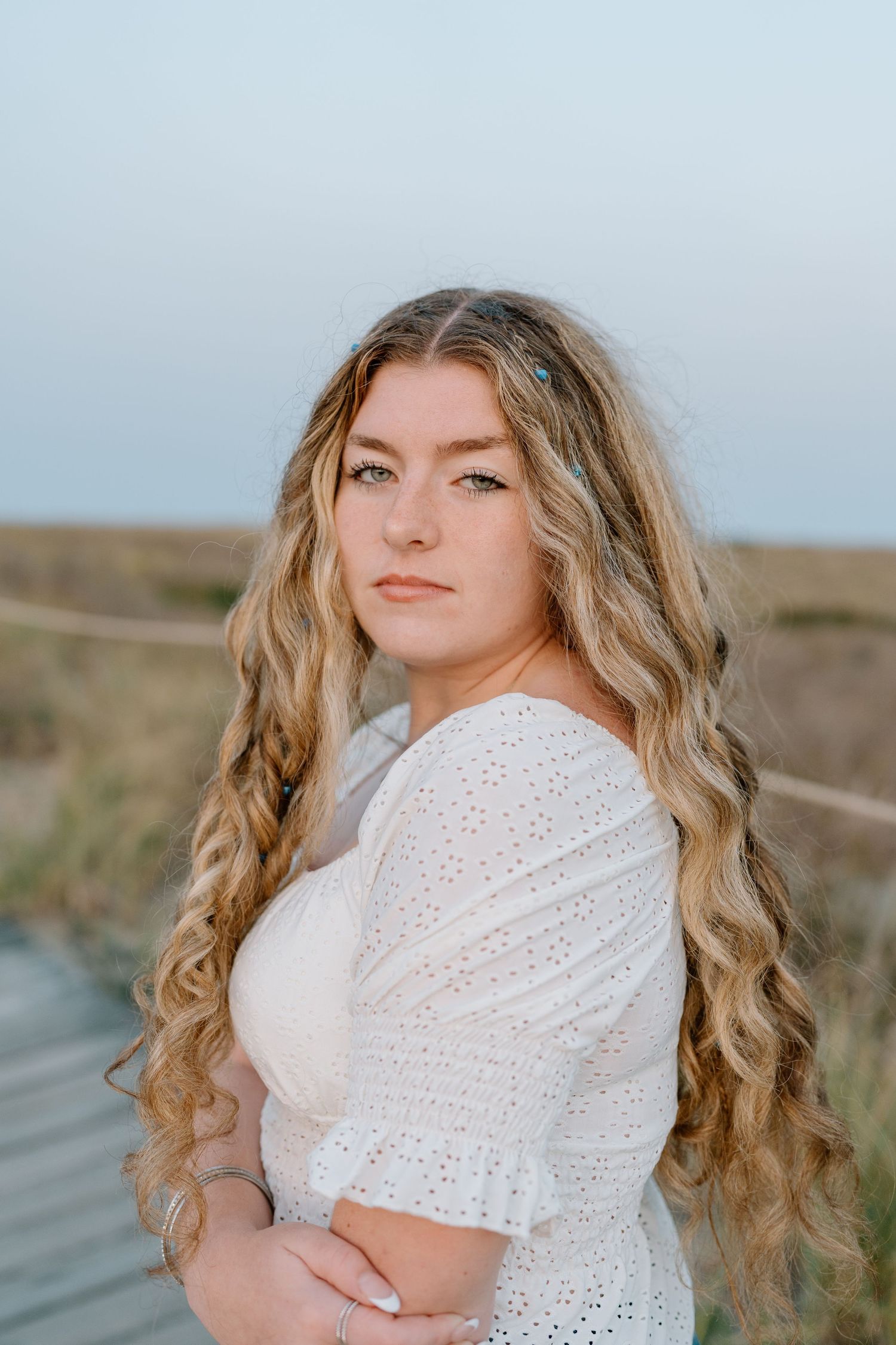 Side portrait showing long wavy hair and white lace top against a natural outdoor background.