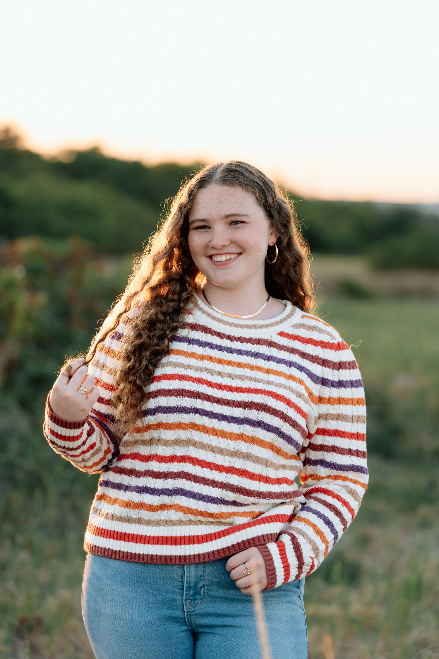 Someone wearing a colorful striped sweater poses in a field during golden hour.