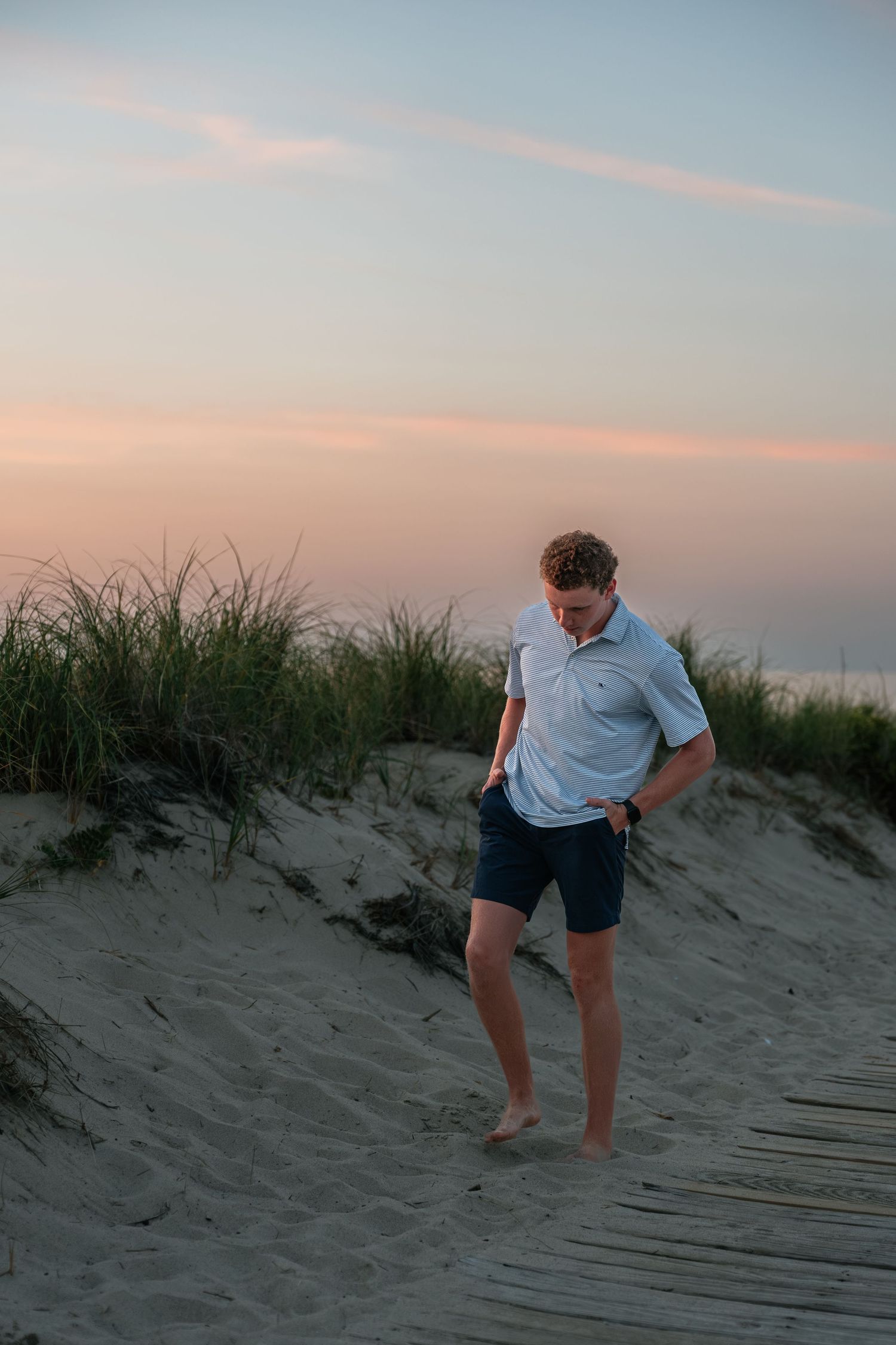 Person in light colored shirt walks up sandy dune steps during sunset.