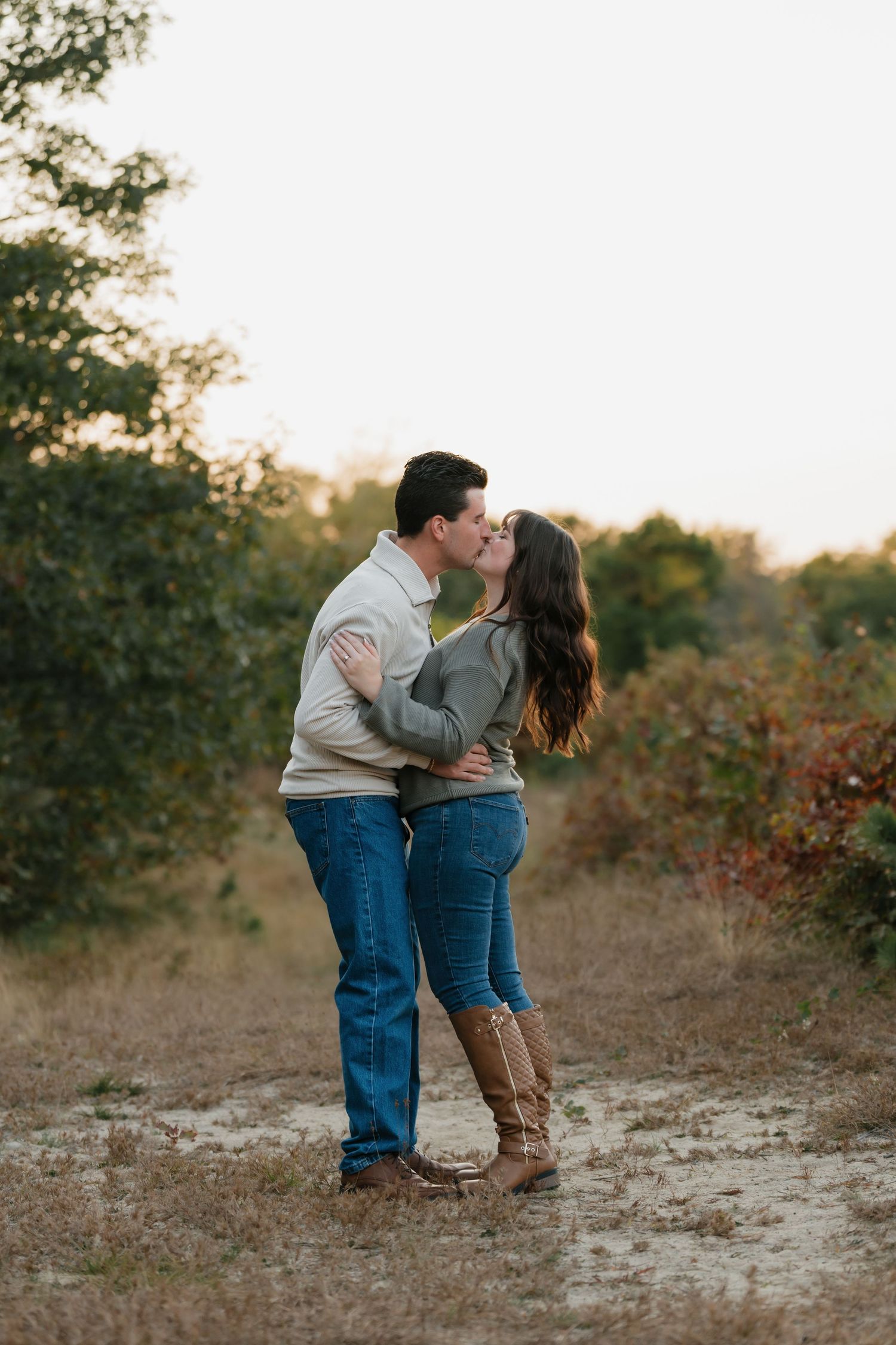 A couple shares a romantic moment on a dirt path surrounded by autumn brush.