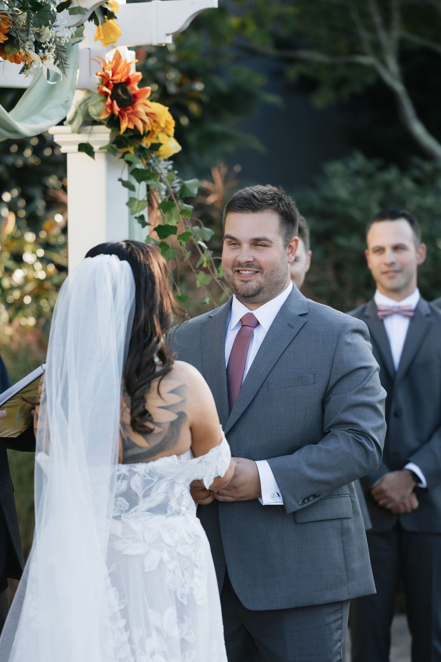 Wedding ceremony moment captured under an arbor with orange and yellow fall floral decorations.