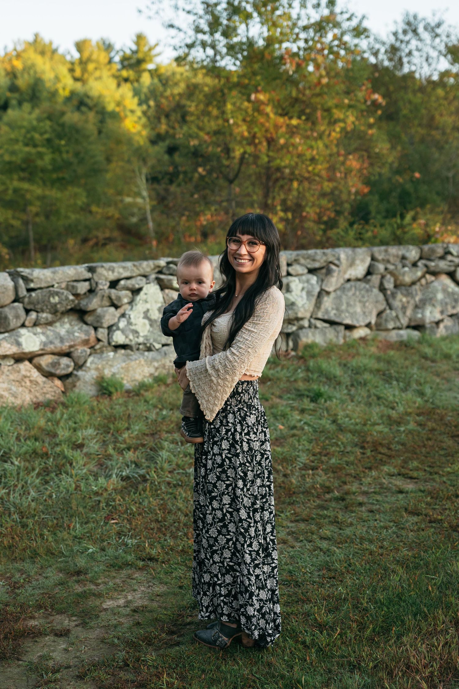 Couple playing hide and seek near an old stone wall surrounded by fall foliage.