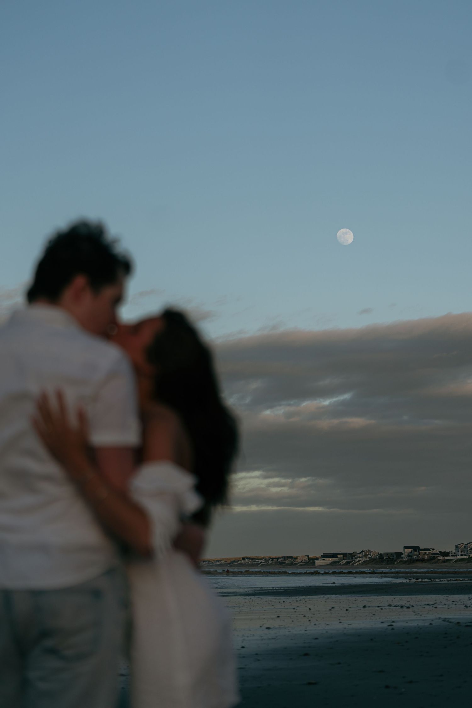 A couple embraces on a moonlit beach with waves crashing in the background.