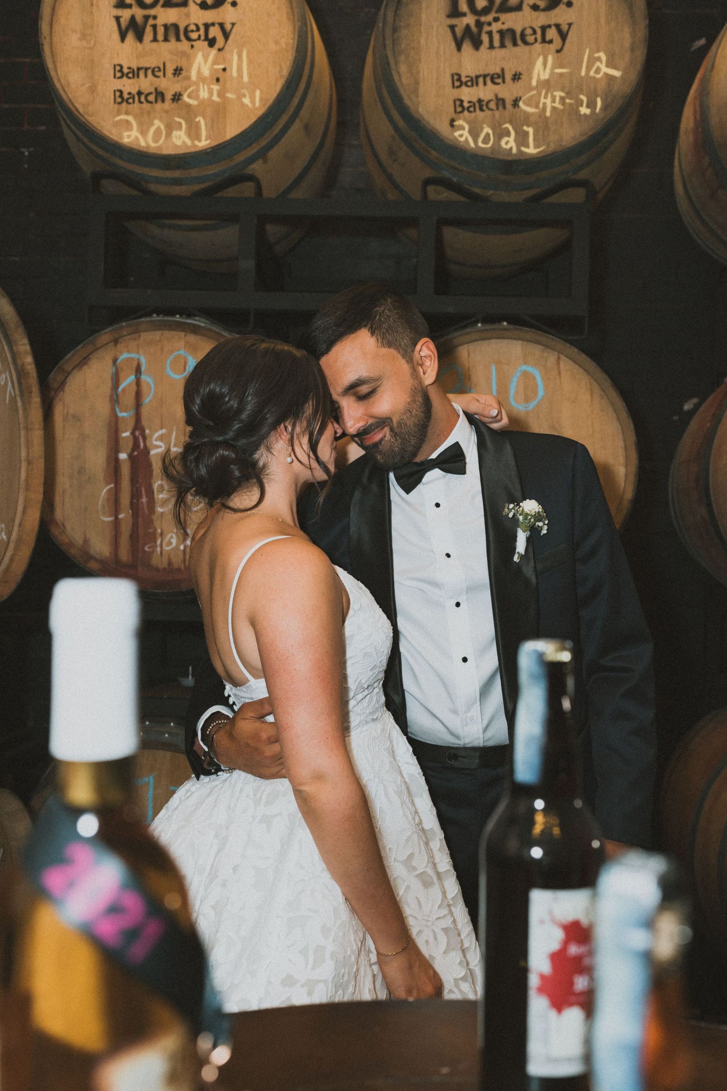 Intimate moment captured between newlyweds among wine barrels in cellar.