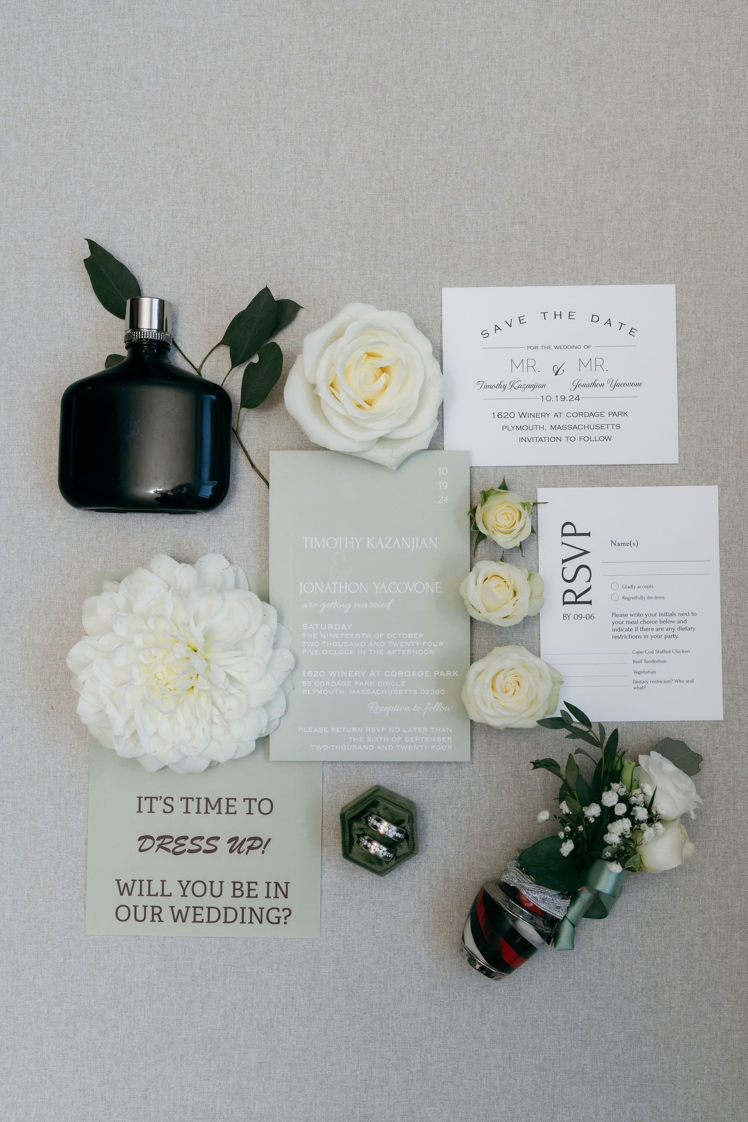 Elegant wedding invitation suite with white roses and greenery on grey background.
