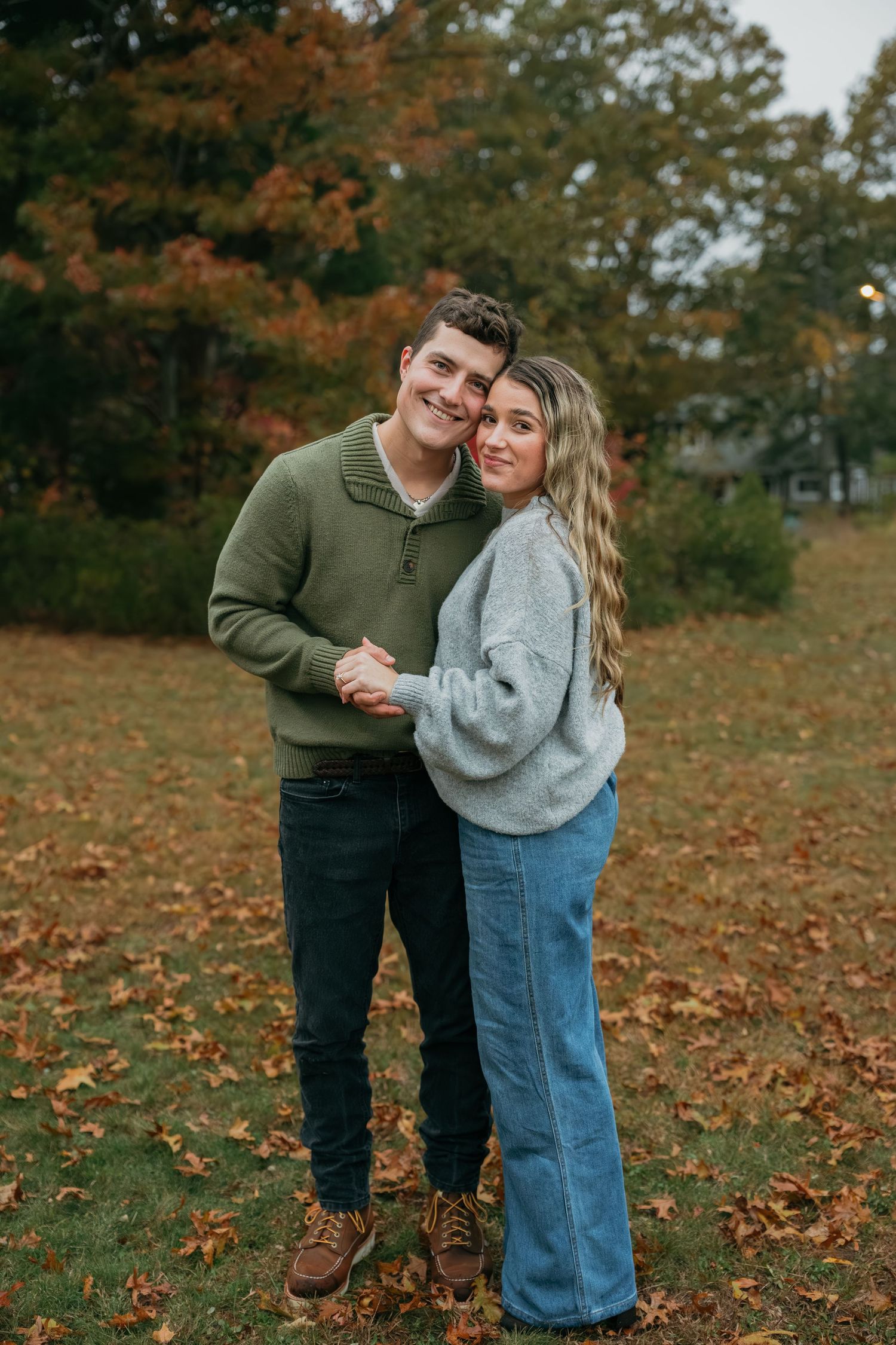 A couple in casual wear poses together on fallen autumn leaves.