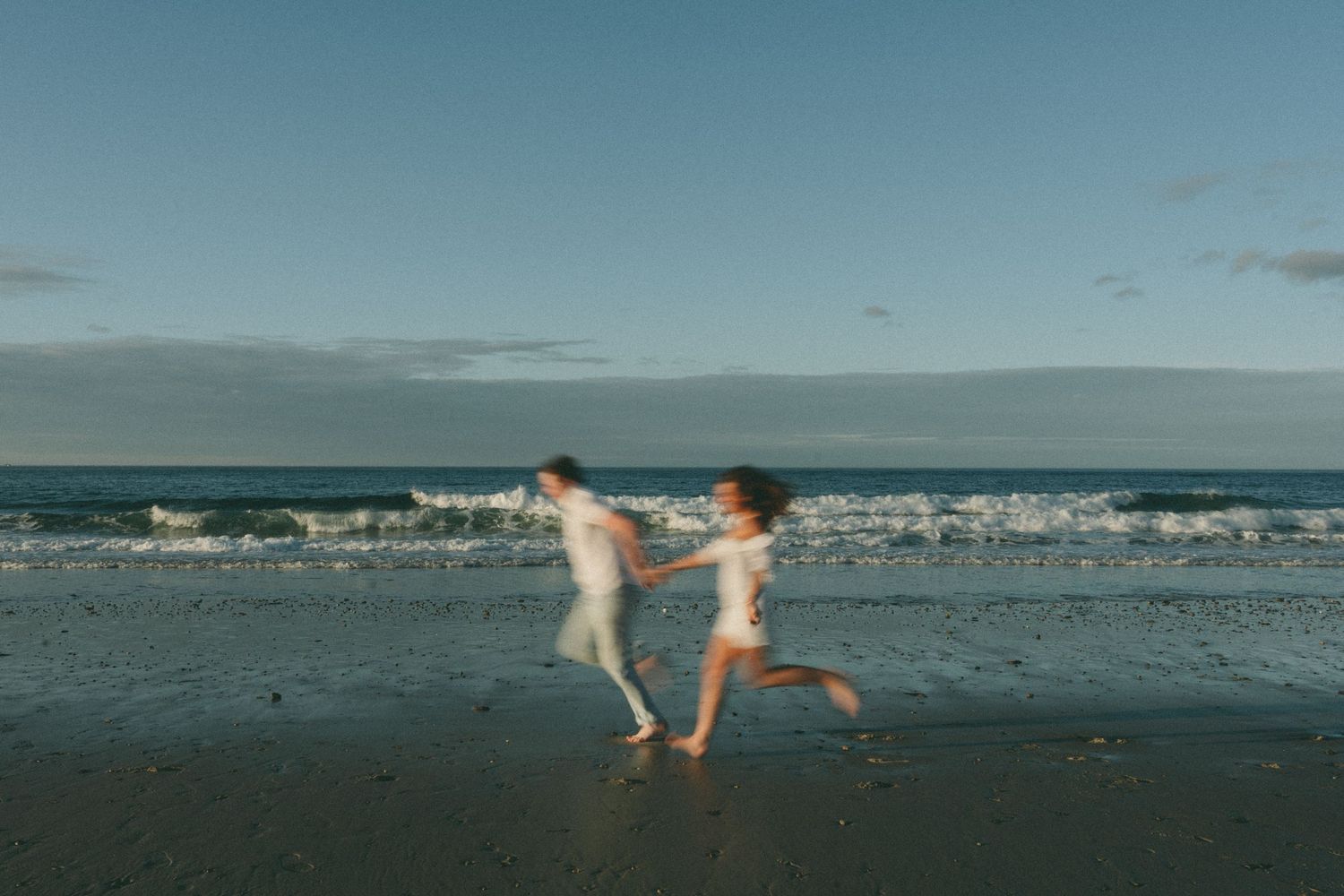 A playful couple runs and dances together on a beach at sunset.