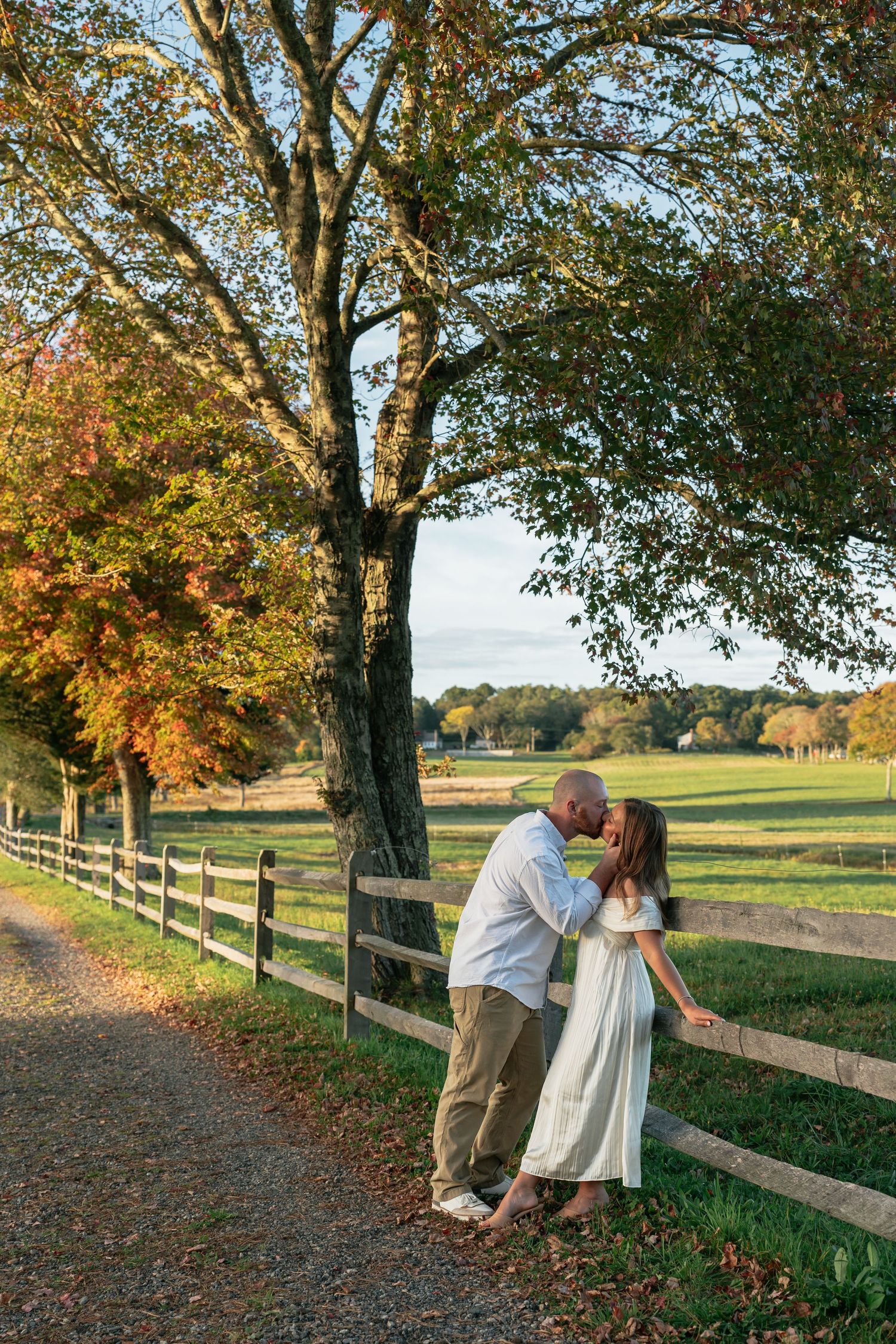 Couple shares intimate moments along tree-lined fence row during autumn sunset.