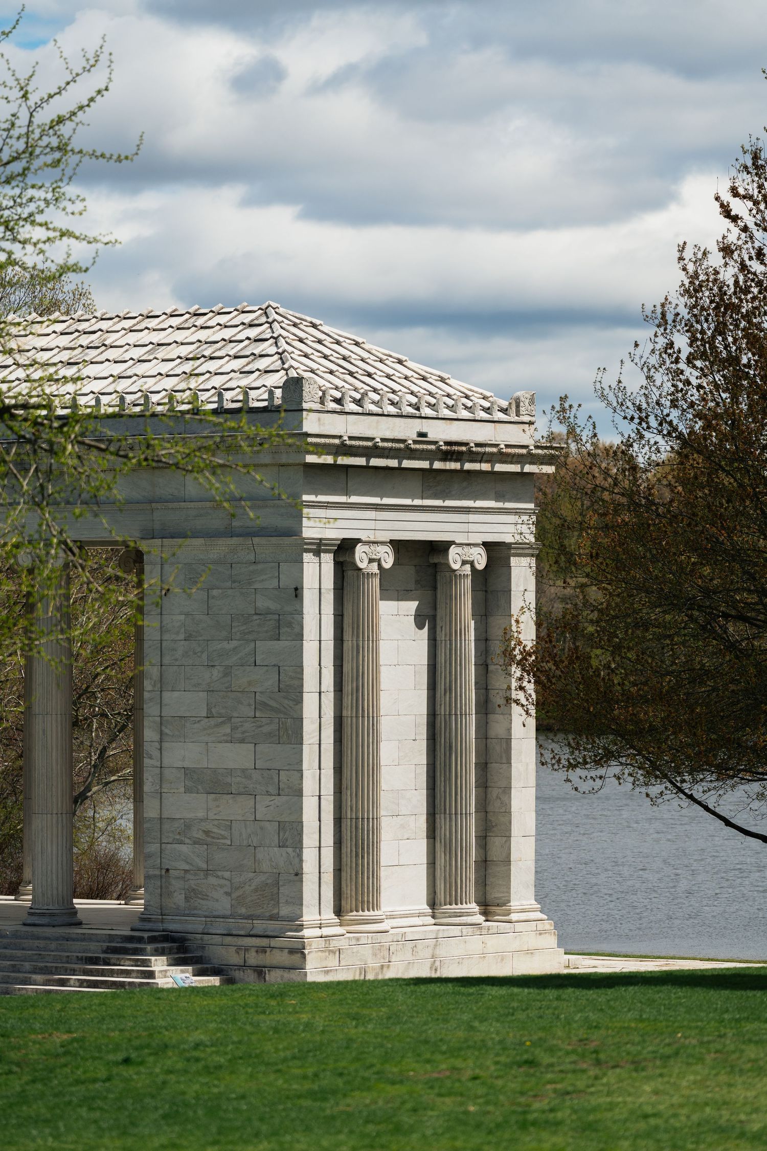 Classical stone pavilion with Ionic columns overlooking a lake on a cloudy day.