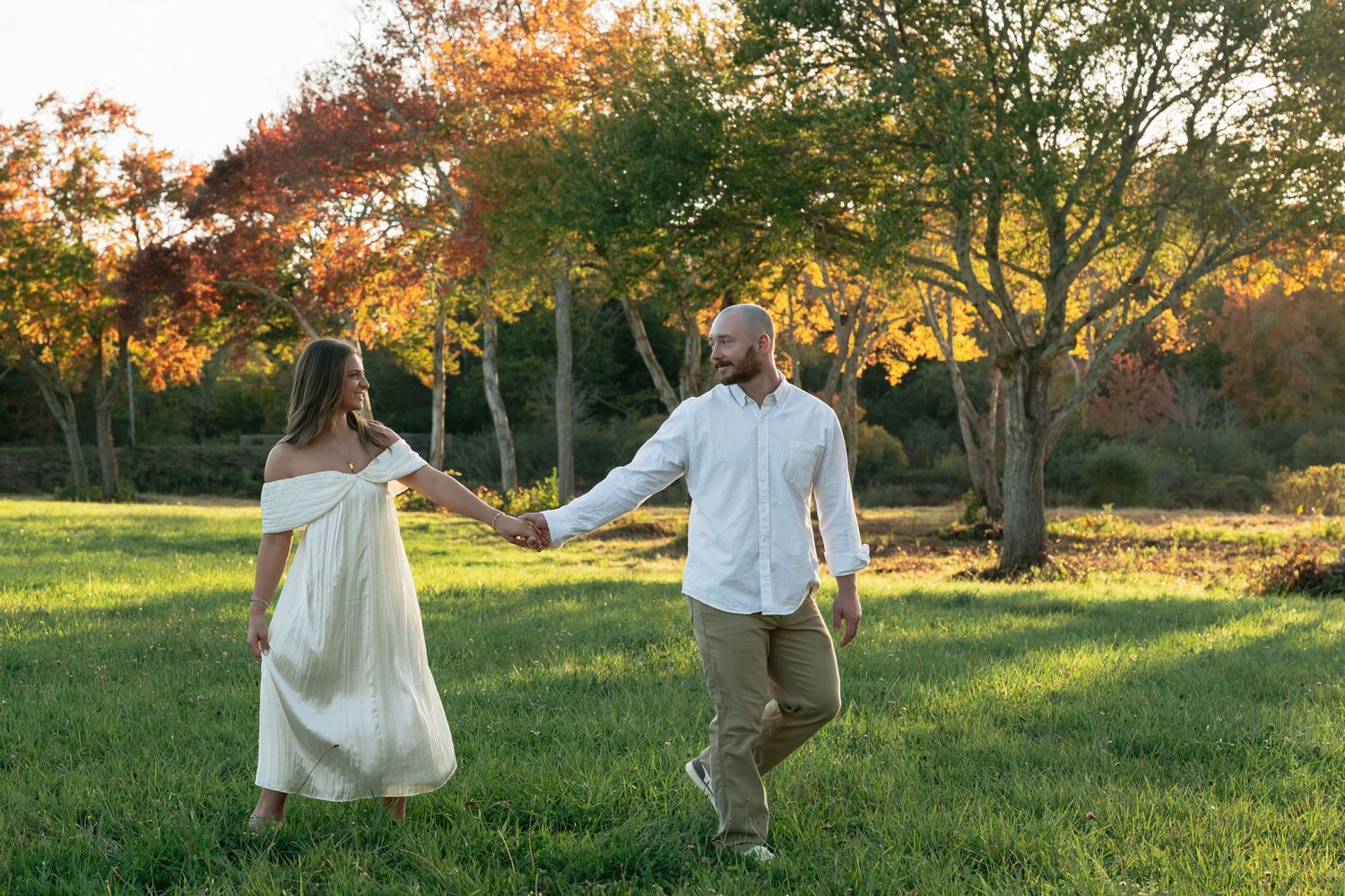 Playful couple twirls together in a grassy field at sunset.