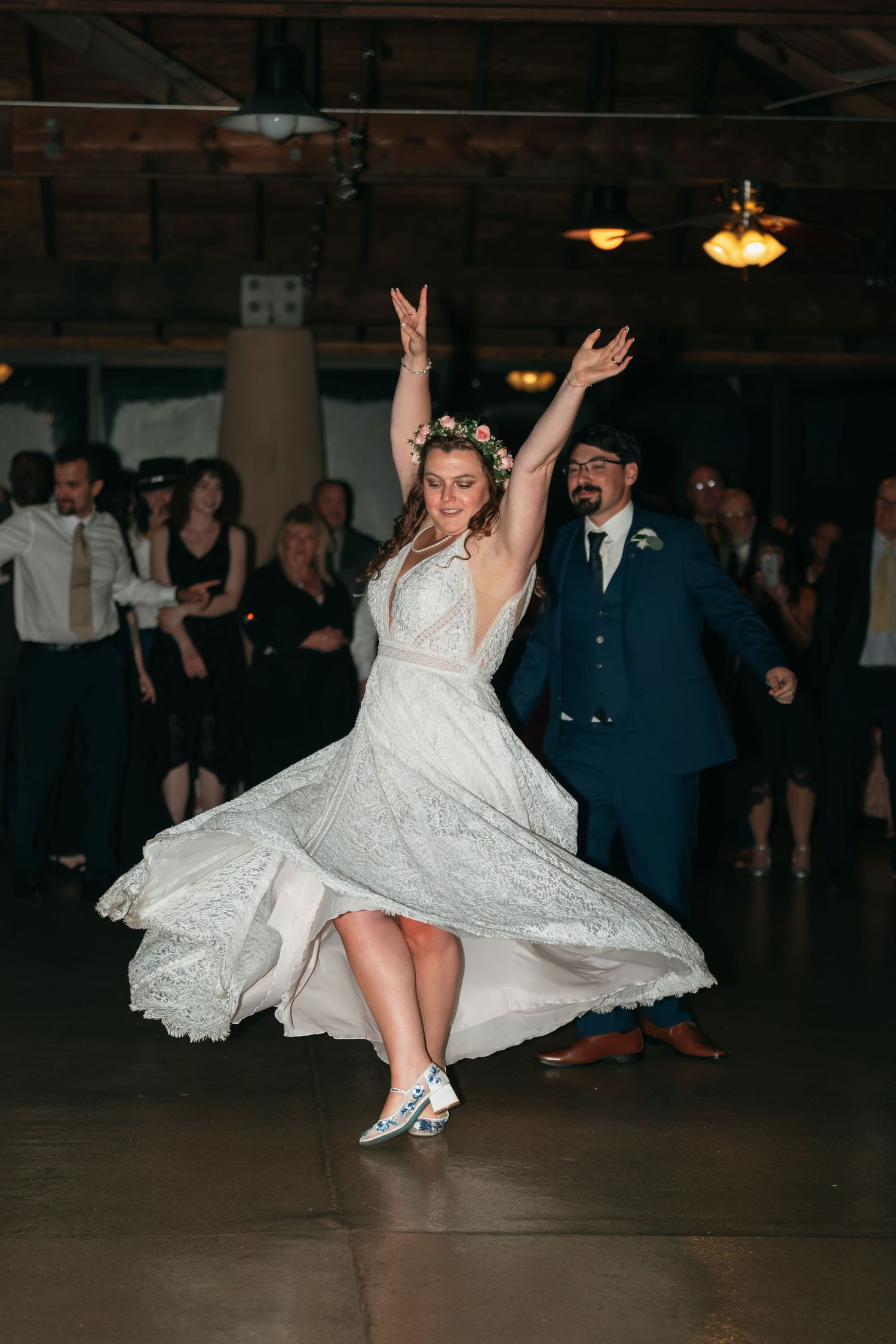 A bride in a lace wedding dress twirls and dances energetically on a dark dance floor.
