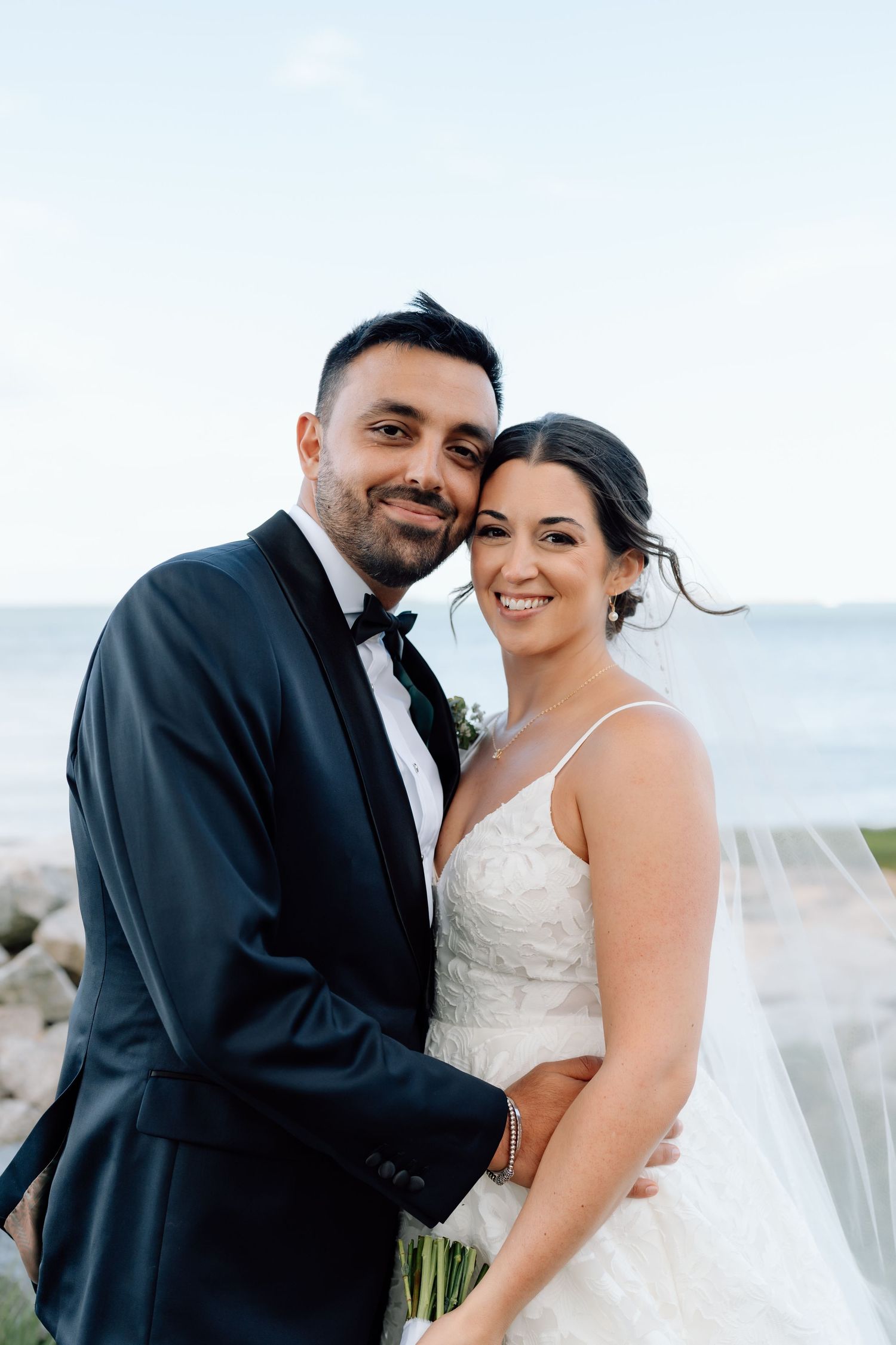 Romantic wedding couple embraces by the ocean during their seaside ceremony.