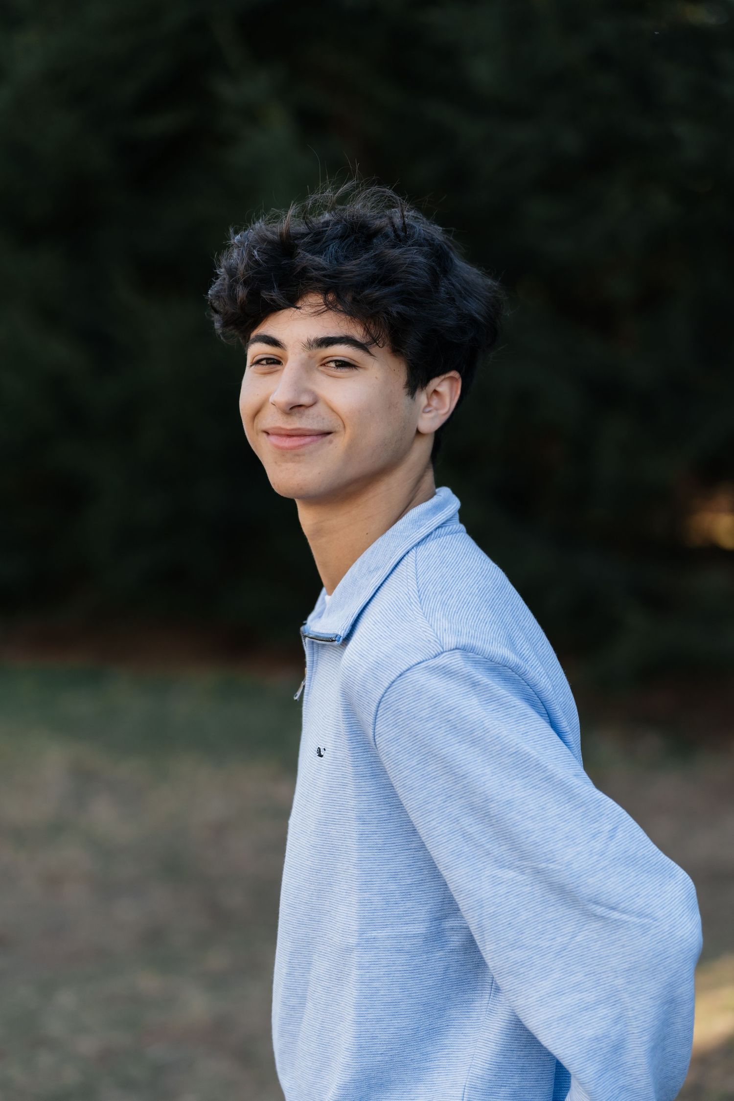 Person in gray sweater smiling during outdoor photo session.