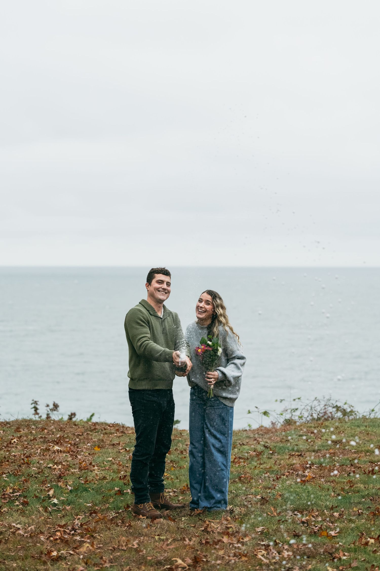 A couple shares a joyful moment together on a coastal cliff overlooking the ocean.