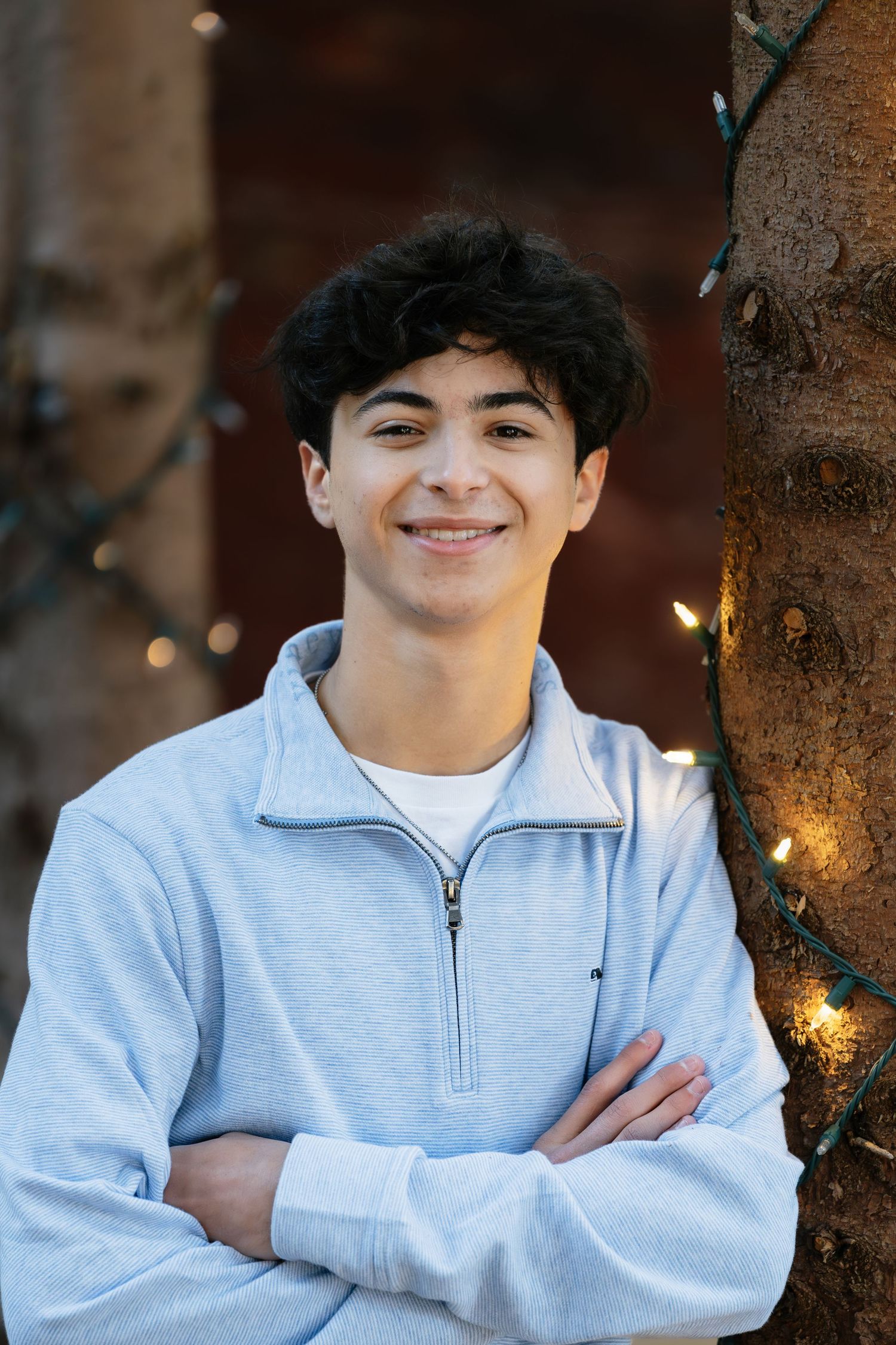 Person in light gray zip-up sweater poses near trees with twinkle lights.