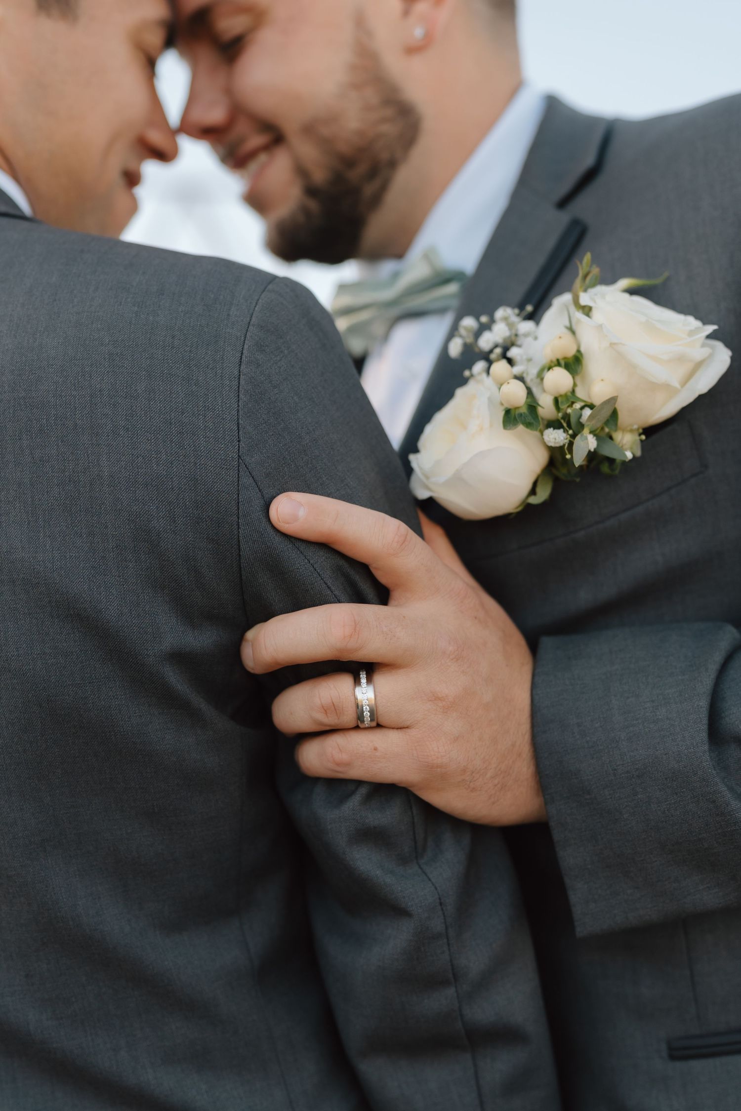 Close-up of white rose boutonnieres and a wedding ring during an intimate moment.