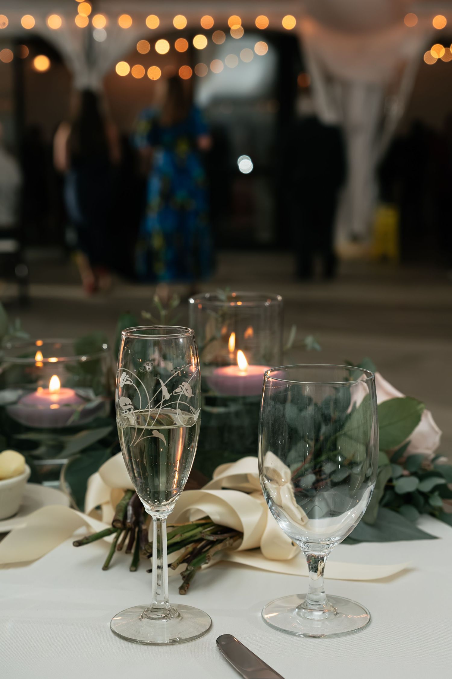 Romantic table setting with champagne glasses, candles and string lights in background.