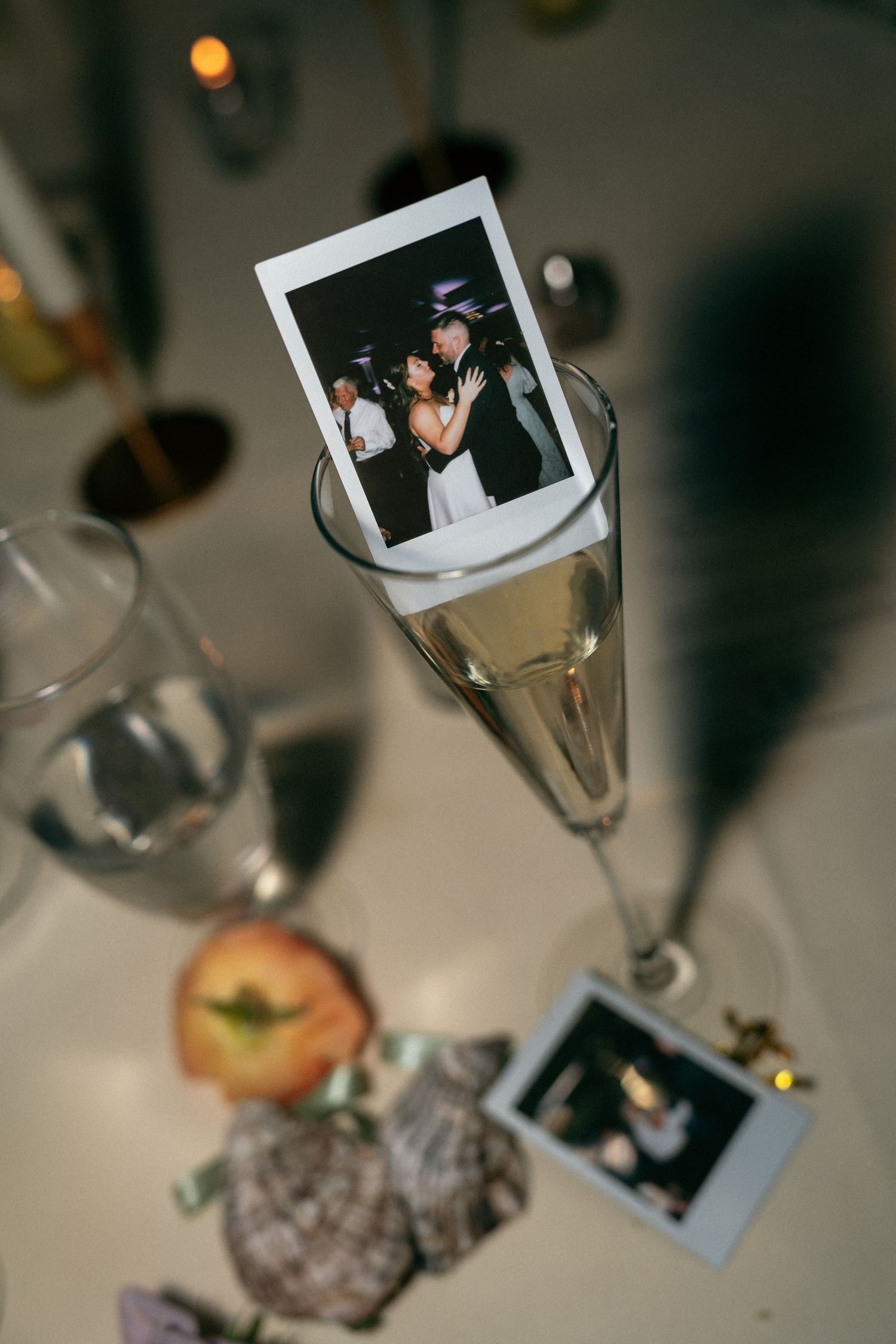 Polaroid wedding photo nestled in champagne flute on decorated table.