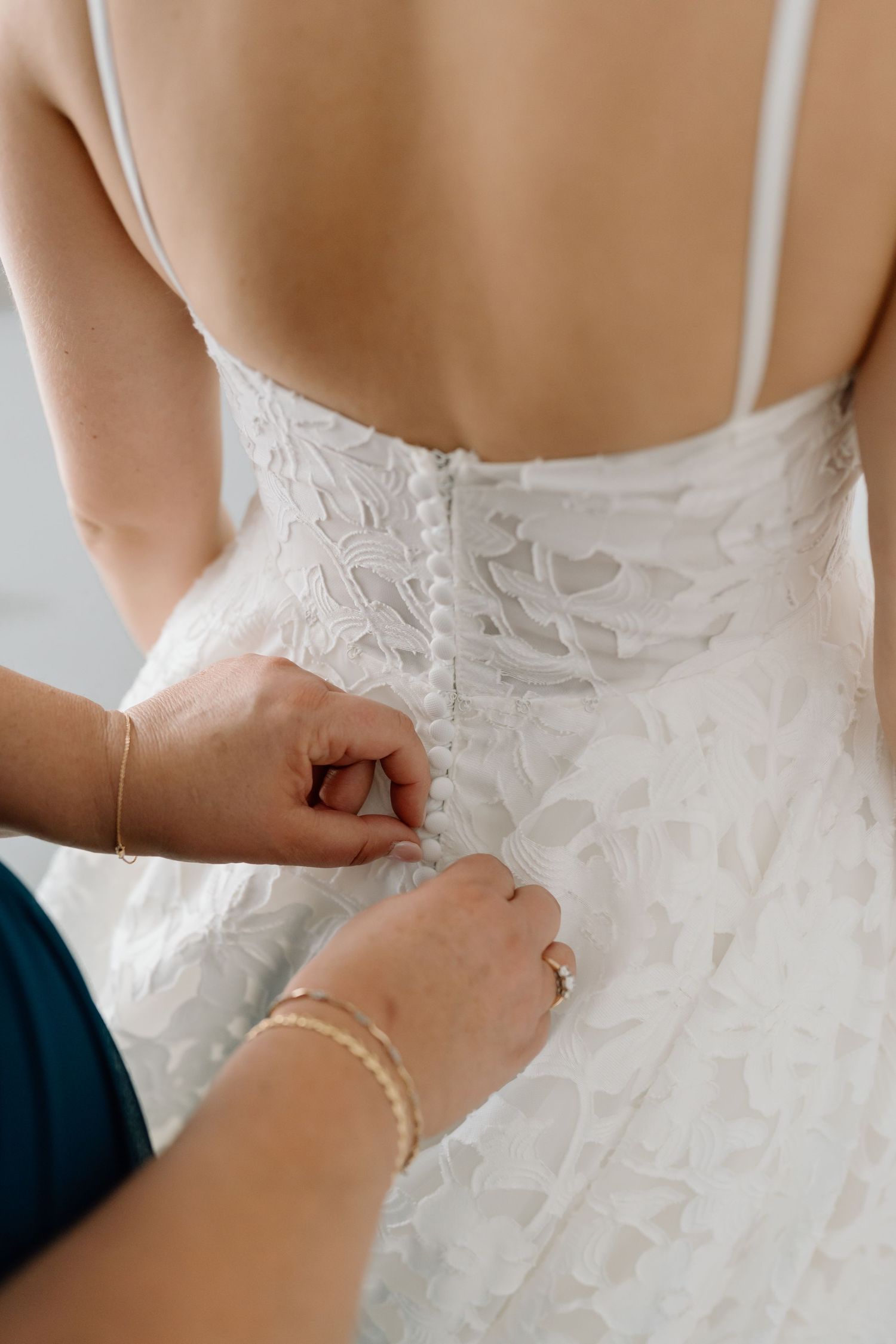 Close-up of hands buttoning up the back of a detailed lace wedding dress.