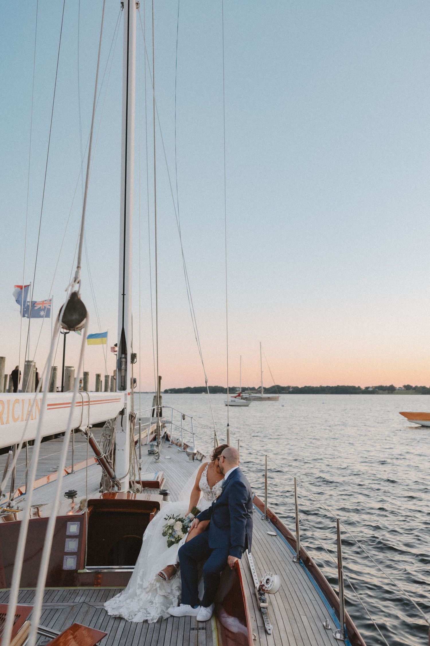 Wedding couple sharing intimate moments aboard a classic wooden sailboat at dusk.