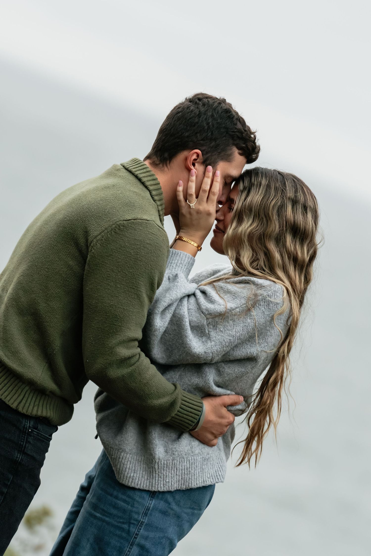 Two people share a close embrace on a cloudy day by the water.