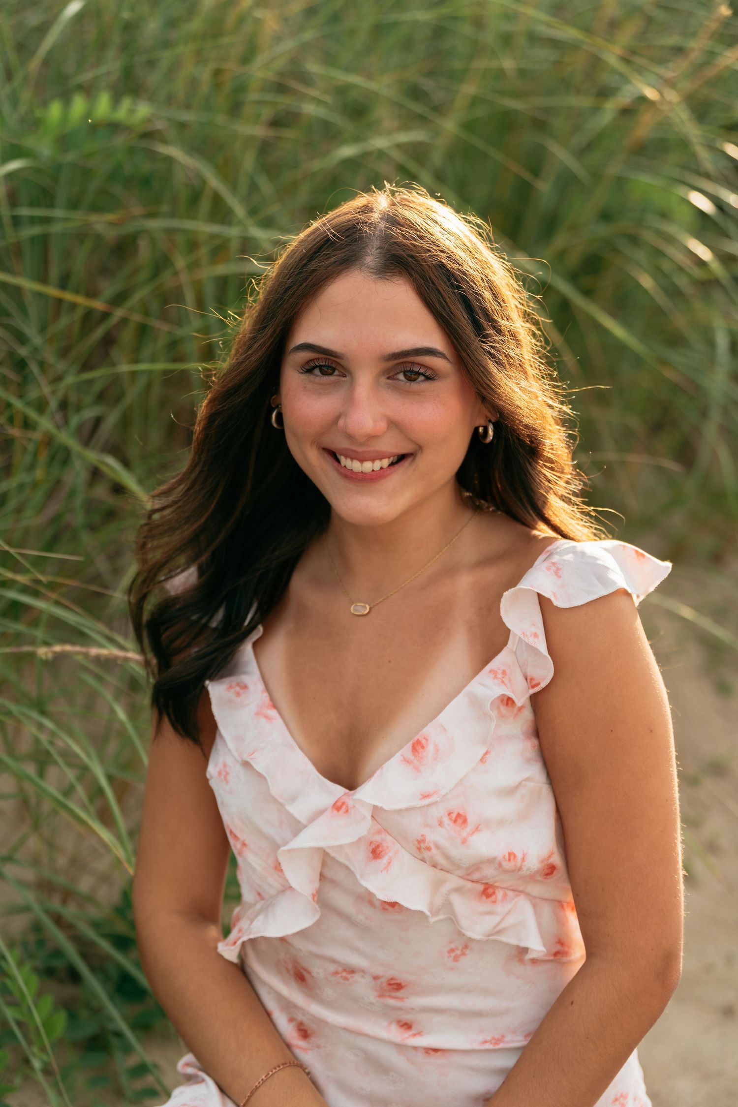 A person in a floral white dress poses in front of tall grass during a photo shoot.
