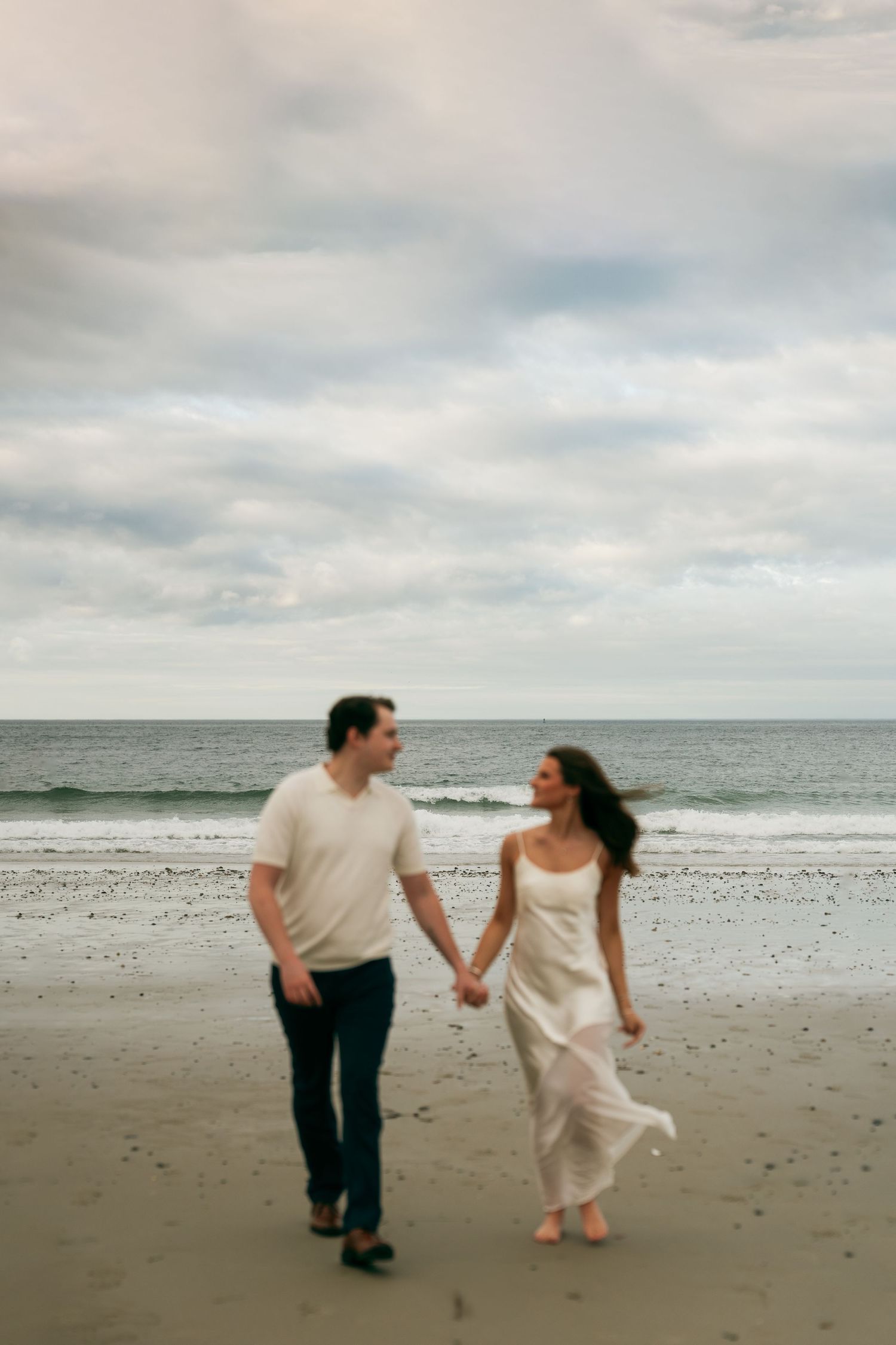 A couple walking hand in hand along a misty beach shoreline.