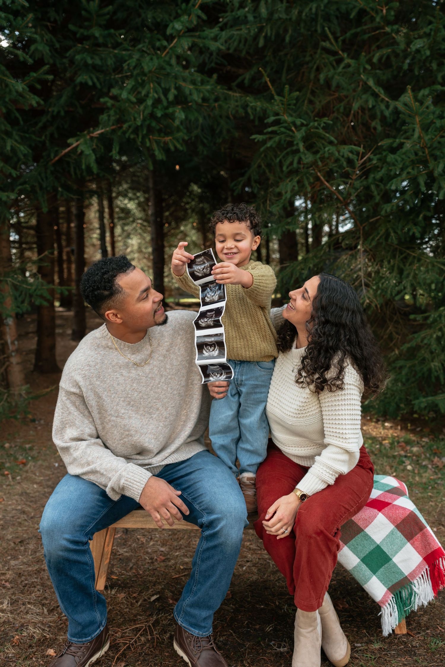 Family sharing joyful moments on a bench with ultrasound photos and holiday blanket.
