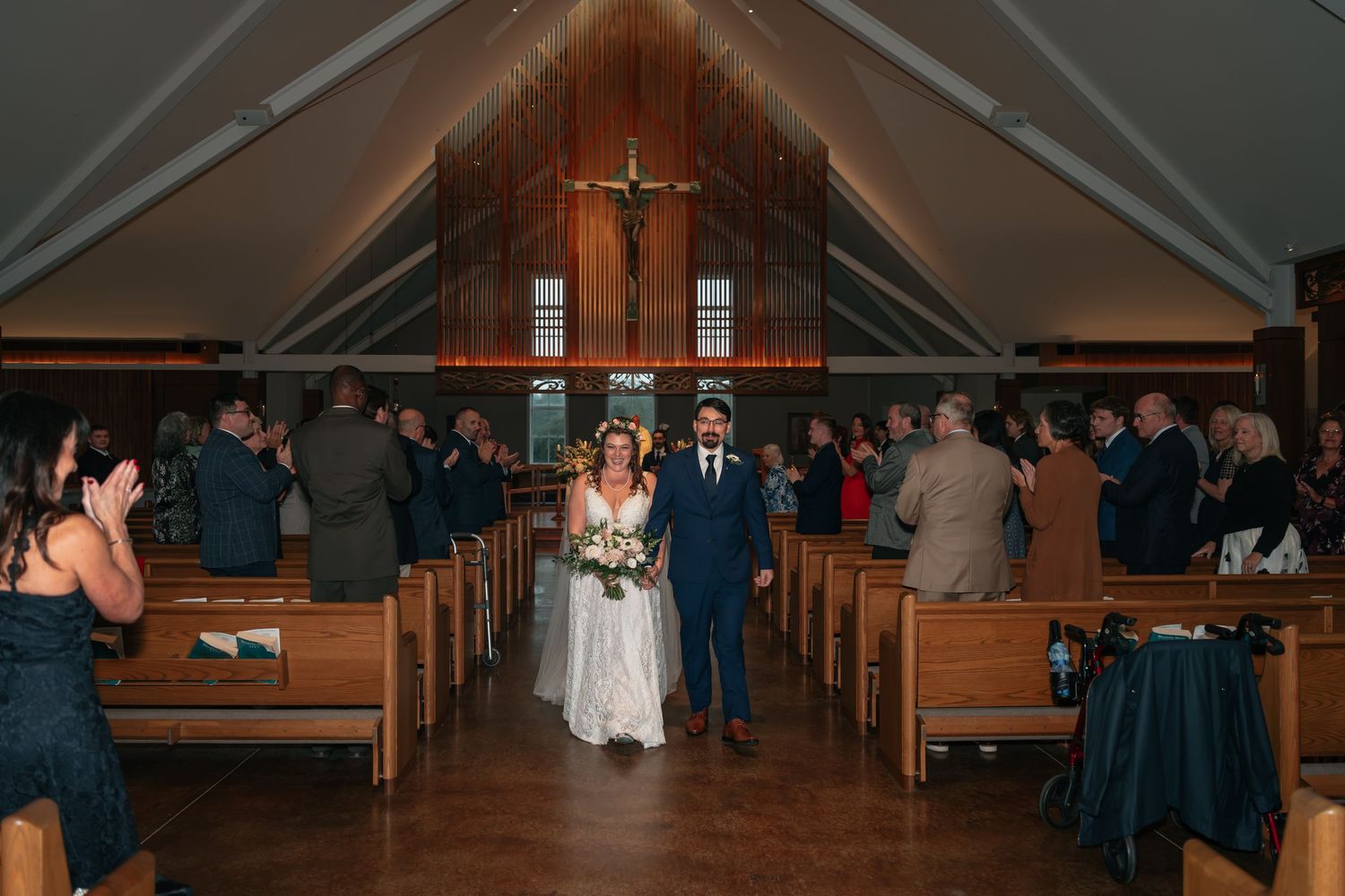 Wide view of a church interior with wooden pews and vaulted ceiling during a wedding ceremony.