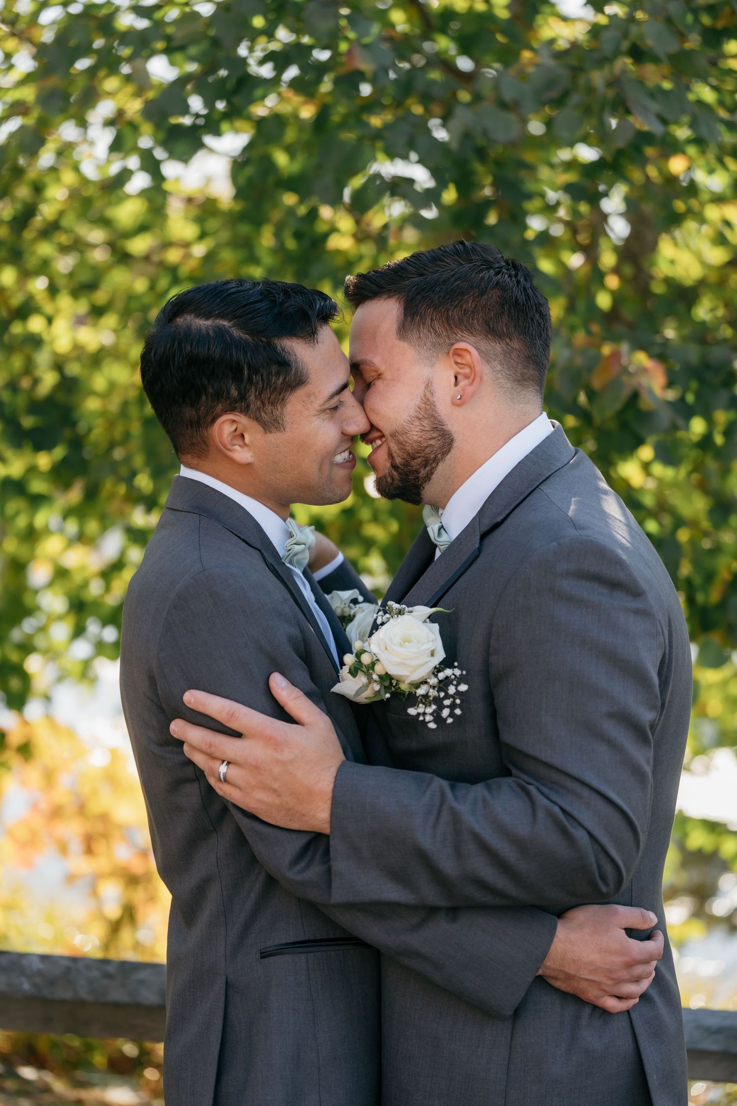 Two grooms in matching gray suits share an intimate embrace during their wedding photoshoot.
