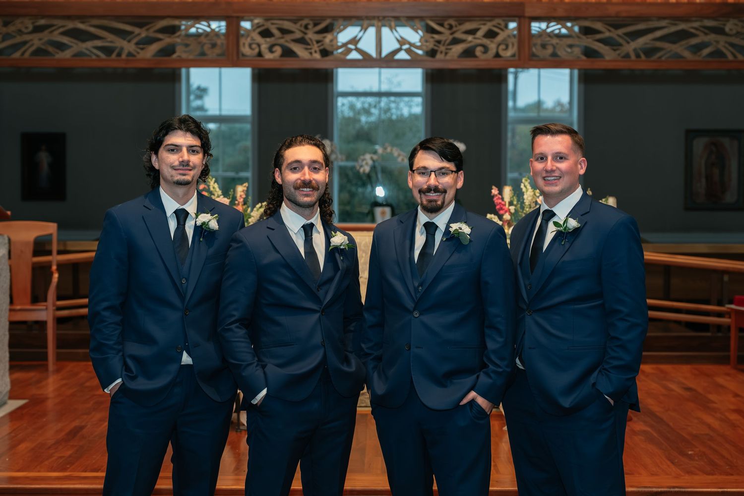 Groomsmen in navy blue suits stand together in front of wooden church interior.