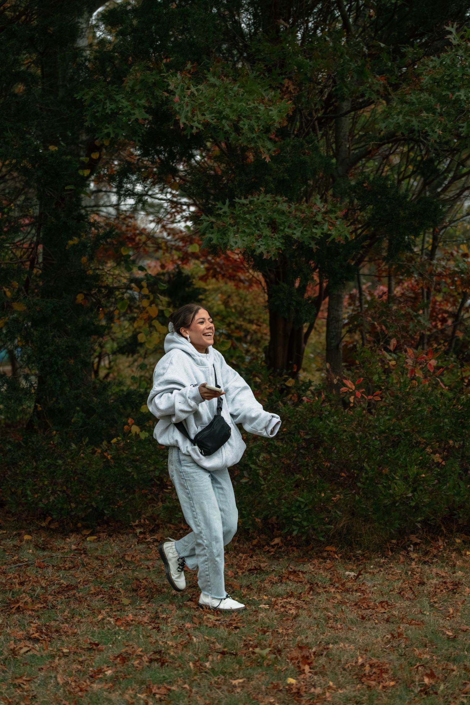 Someone jumping playfully through autumn leaves in a wooded area.