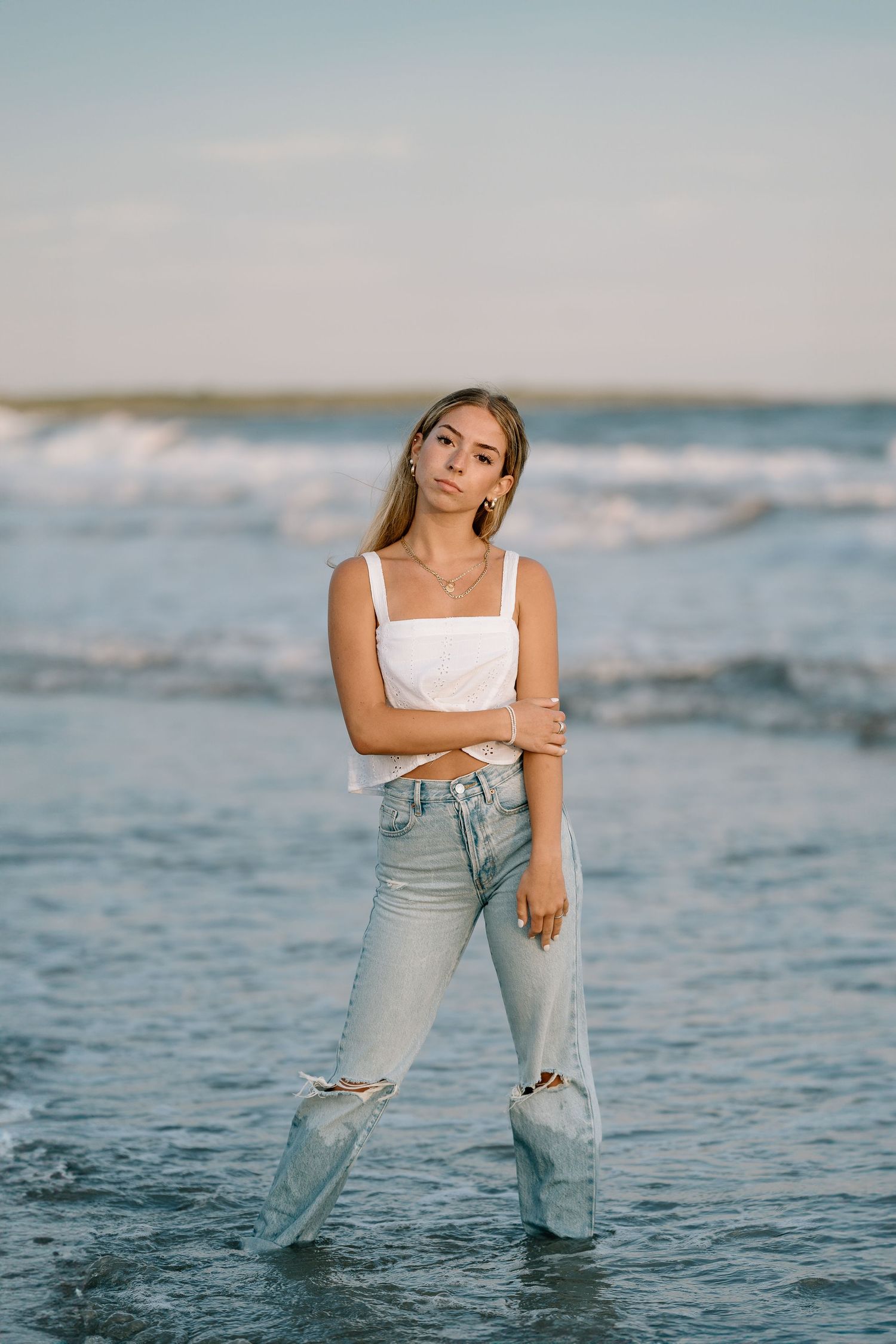 Person splashing in ocean waves wearing distressed jeans and white tank top.