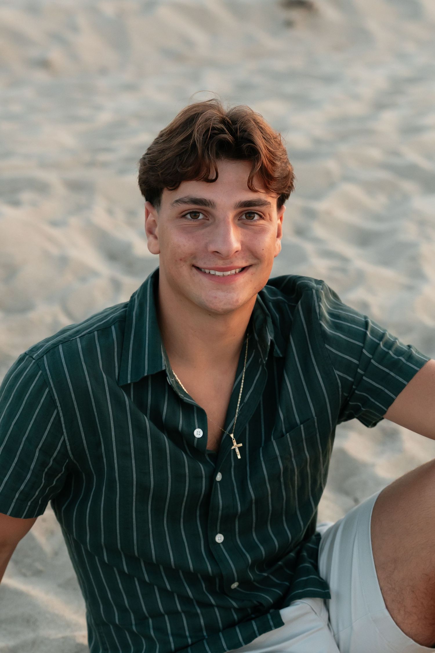 Person in dark striped shirt sits on sandy beach during golden hour photography session.