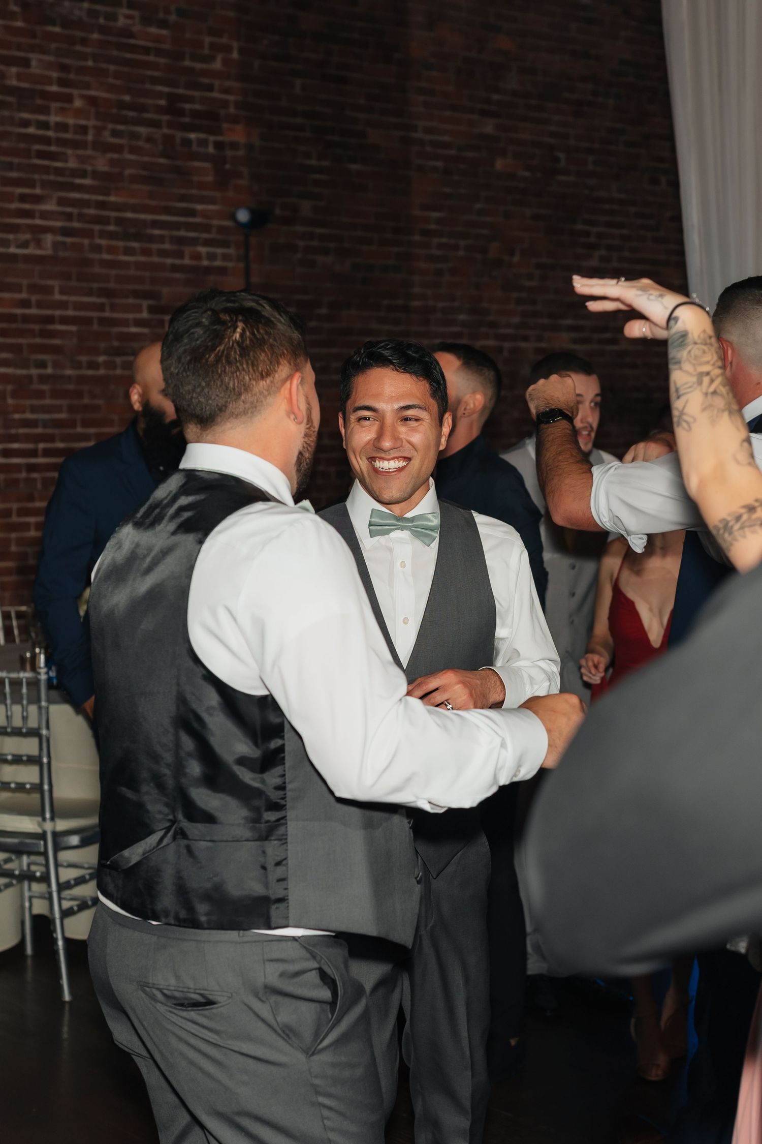 Wedding party members dancing and celebrating in formal attire at indoor reception.