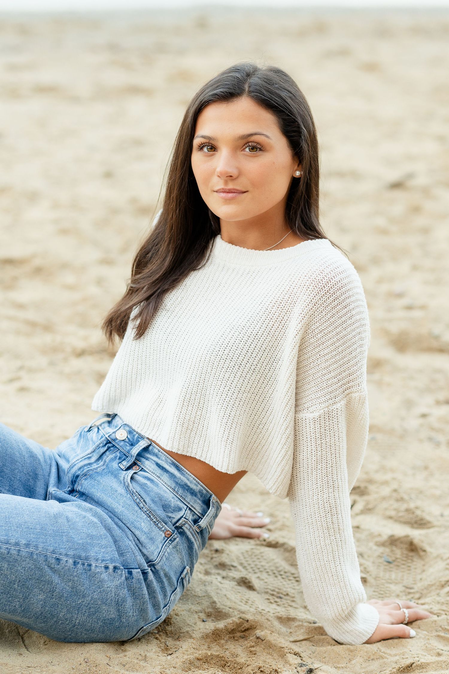 Beach portrait with white sweater and denim in relaxed pose.