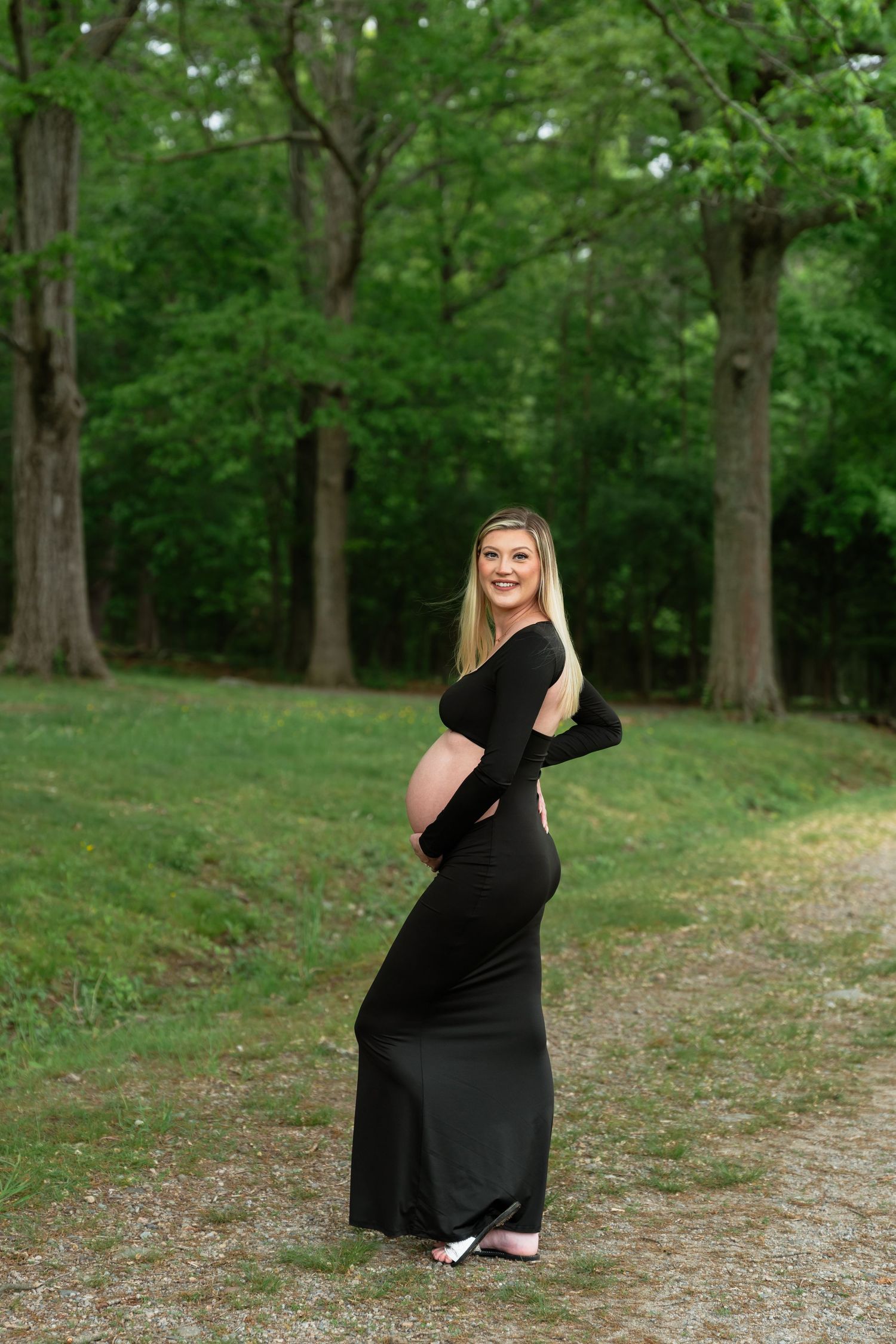 Maternity photos in a lush green park setting with woman in black dress.