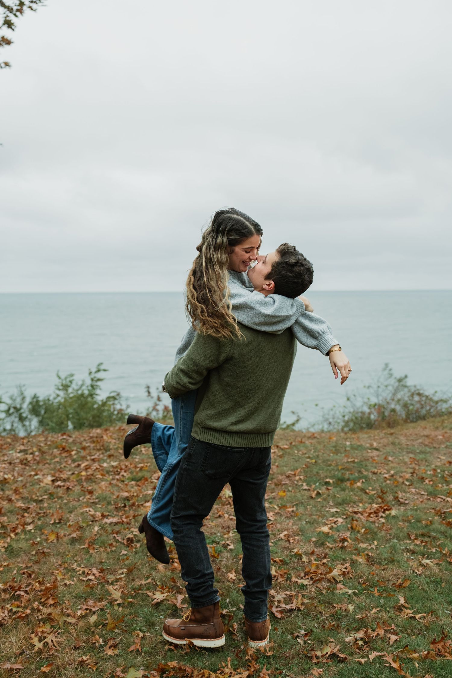 A couple dances and embraces on a grassy slope during fall.